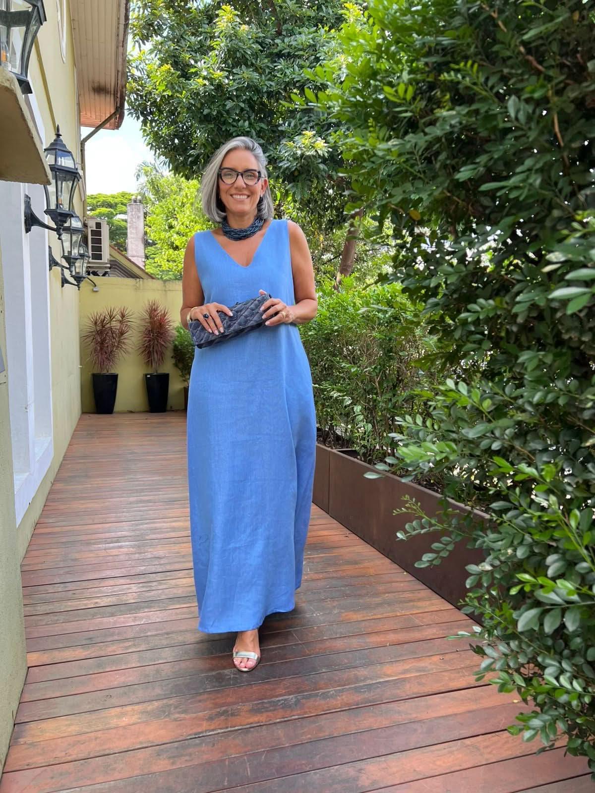 Mulher sorridente usando vestido longo azul de linho em varanda ao ar livre com plantas EZILDINHA