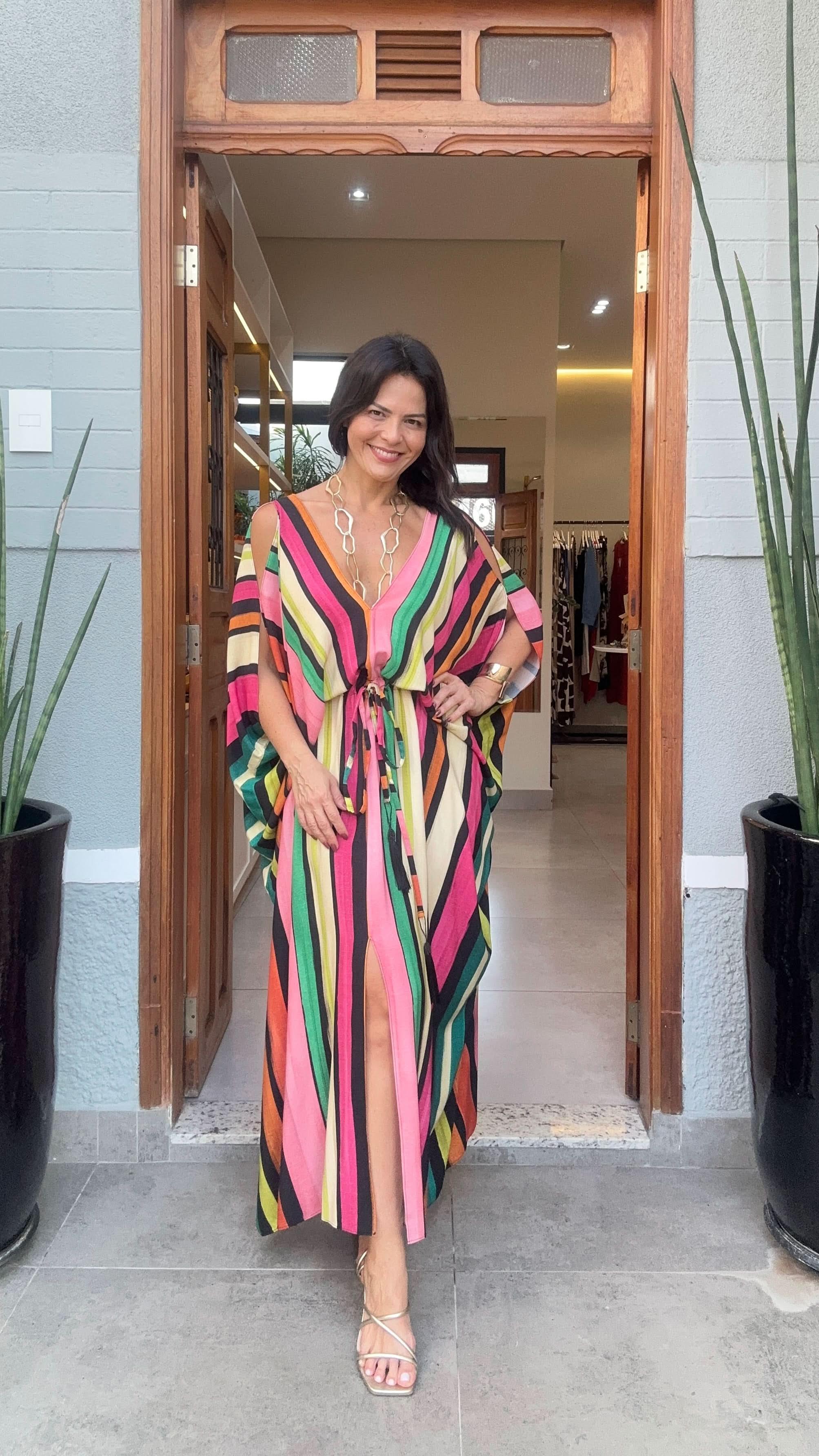 Mulher usando kaftan longo listrado colorido com fenda, em frente a loja de moda feminina EZILDINHA