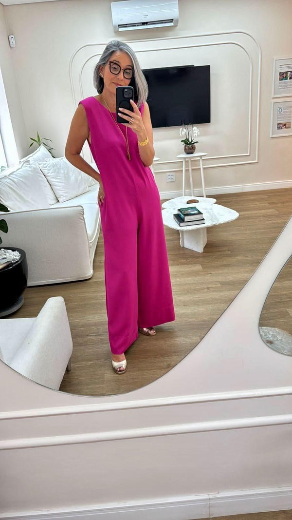 Mulher com macacão pink de linho, posando em sala elegante com sofá e mesa de centro EZILDINHA