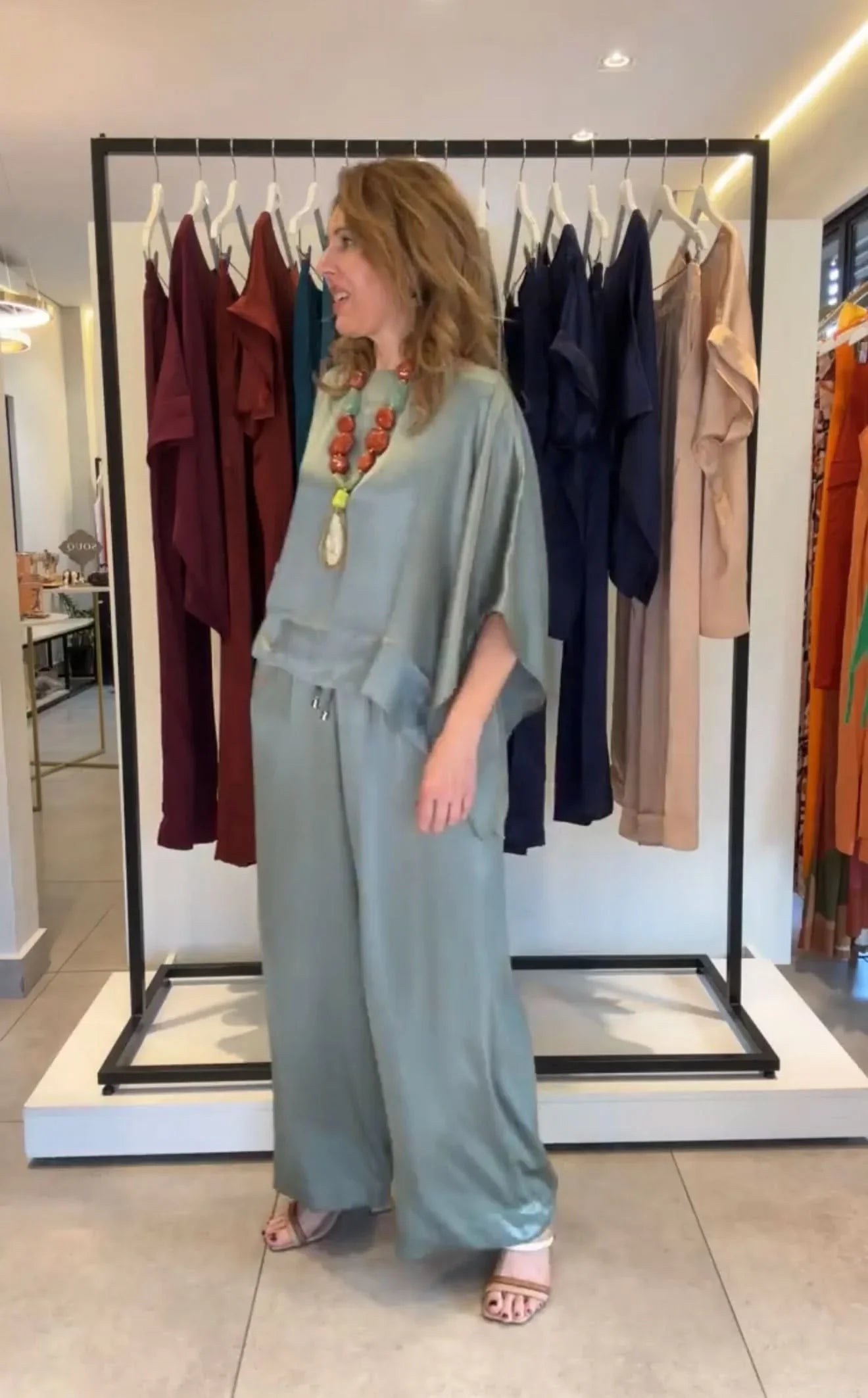 Mulher usando conjunto de viscose verde claro com calça ampla e blusa, colar marcante, em loja de roupas elegantes EZILDINHA