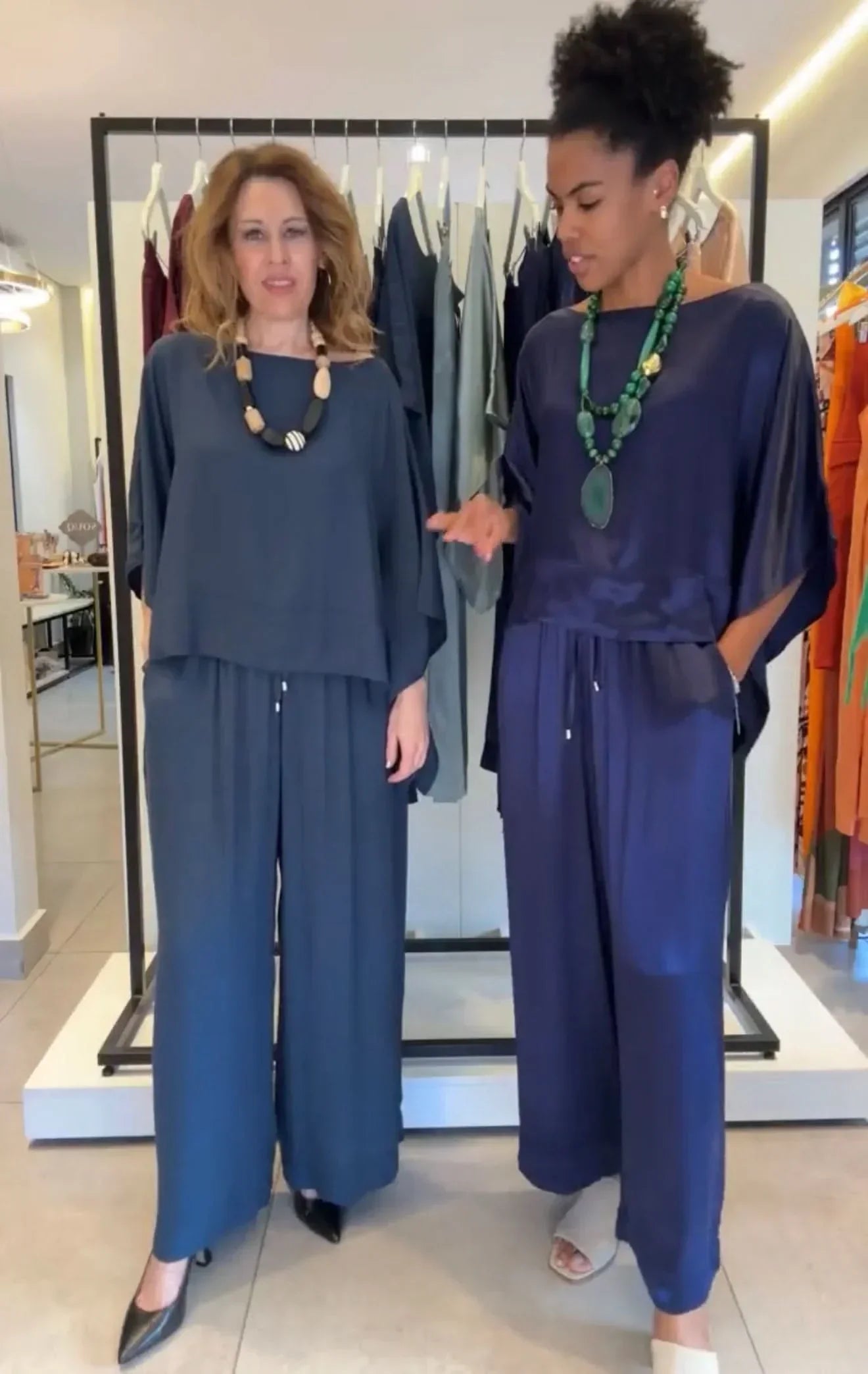 Duas mulheres usando conjuntos de kimono de viscose, calça larga e blusa de manga longa, em tons azul e marinho, com colares grandes, em loja de moda feminina EZILDINHA