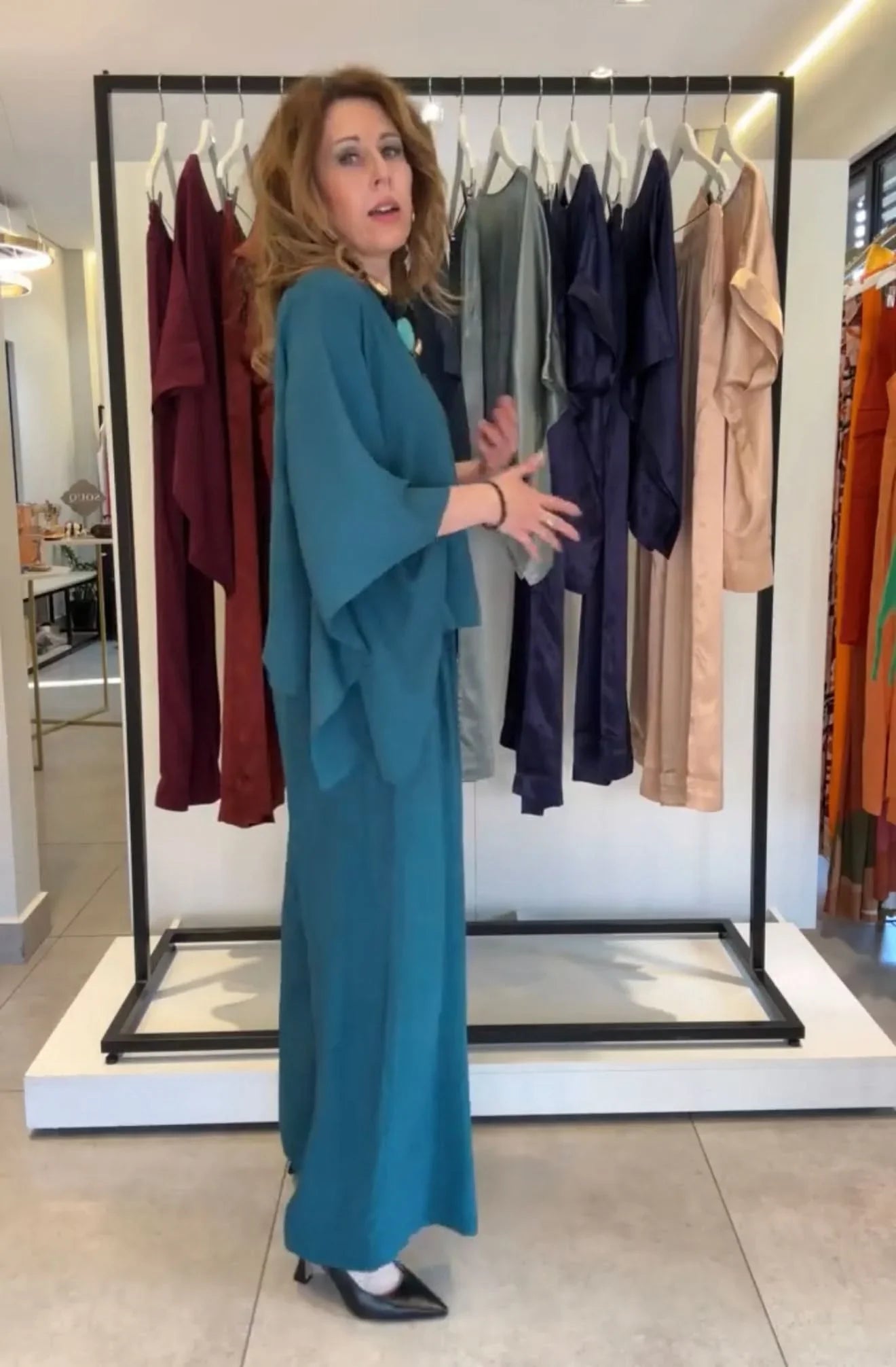Mulher usando conjunto kimono de viscose azul em loja, roupas elegantes penduradas ao fundo EZILDINHA