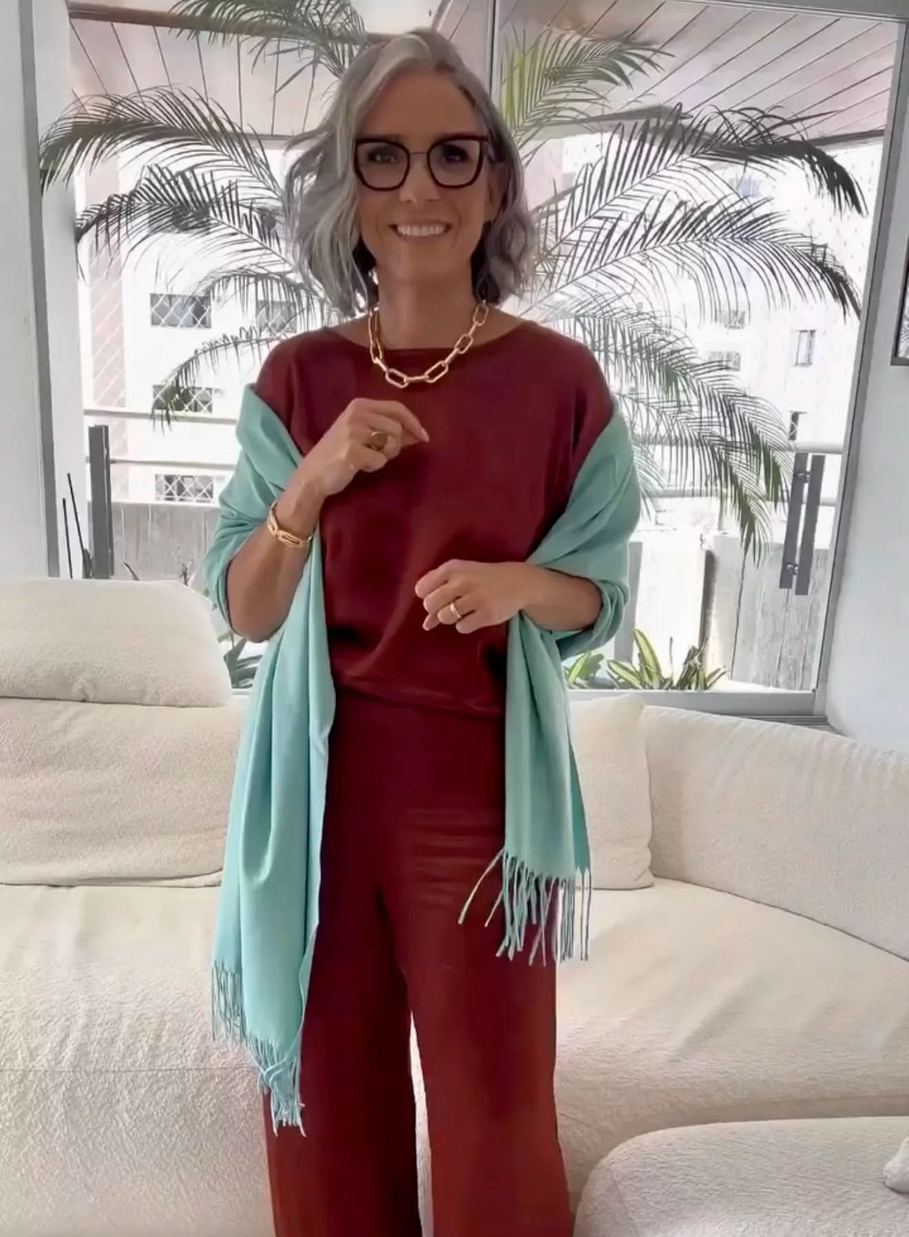 Mulher com cabelo grisalho usando conjunto de linho vinho e echarpe azul em sala moderna EZILDINHA