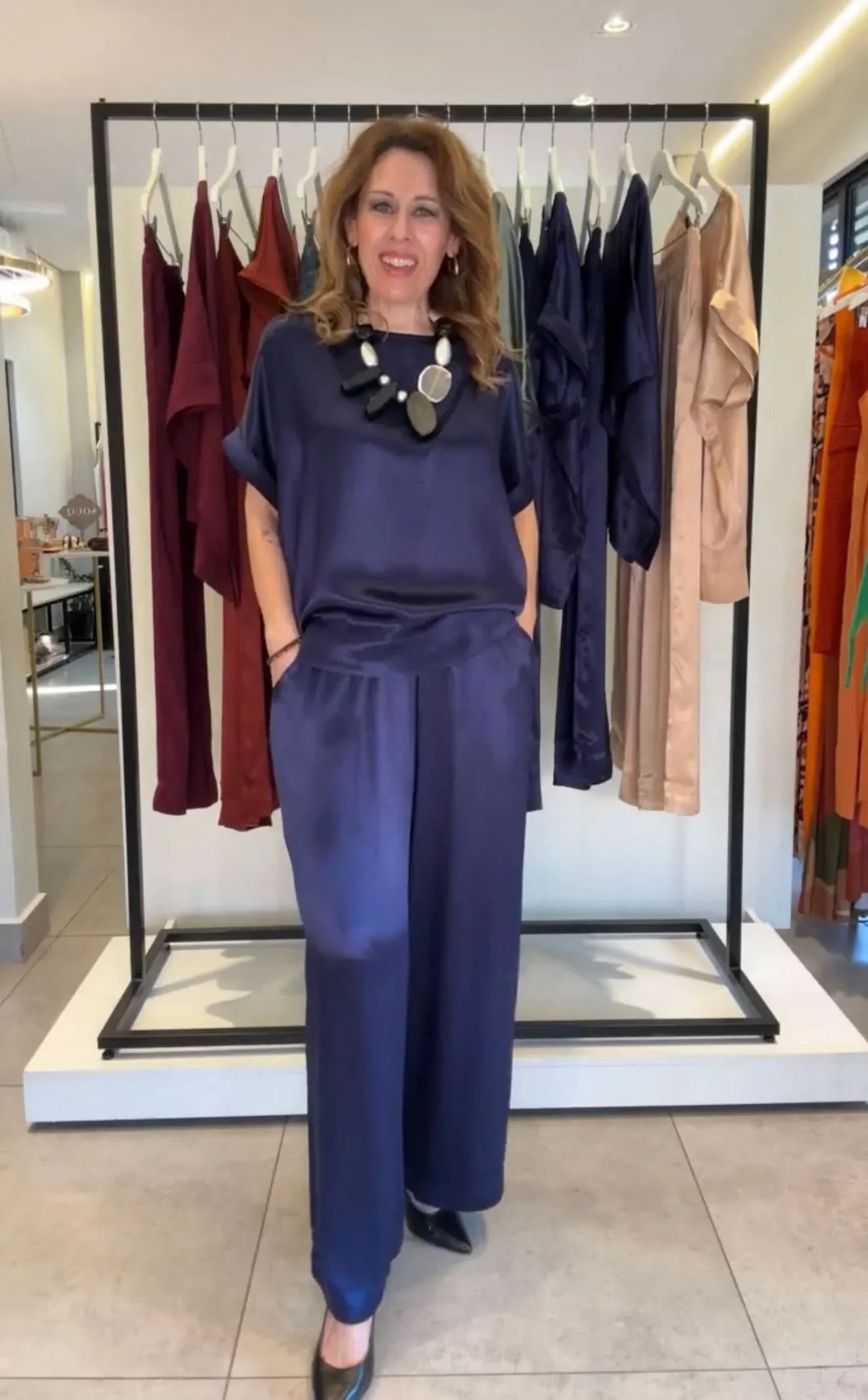 Mulher usando conjunto pantalona azul de manga japonesa, fundo araras com roupas elegantes EZILDINHA