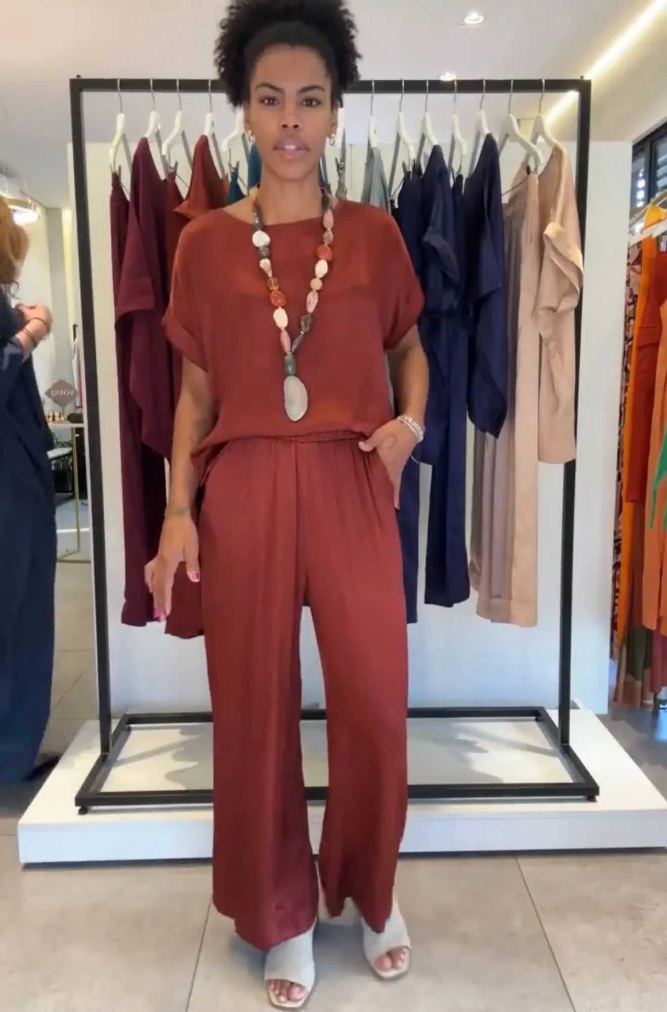 Mulher vestindo conjunto pantalona manga japonesa terracota, colar de pedras, em loja de roupas EZILDINHA