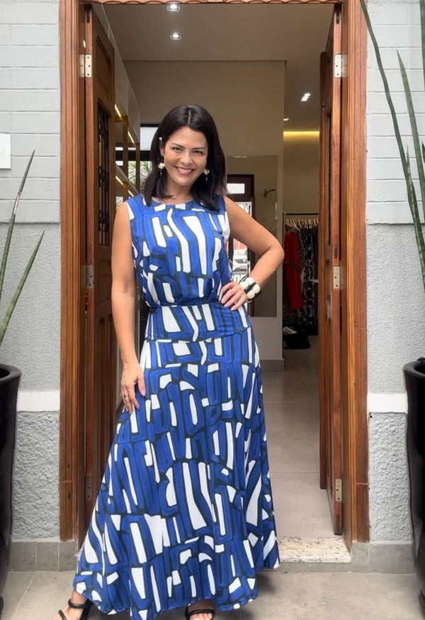 Mulher com conjunto de saia longa azul e branca geométrica, em ambiente elegante EZILDINHA
