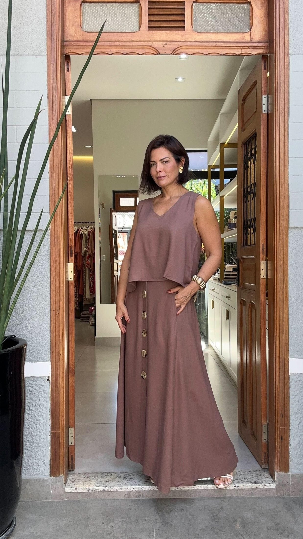 Mulher usando conjunto de saia longa e blusa de viscose marrom, com botões decorativos, em ambiente interno iluminado EZILDINHA