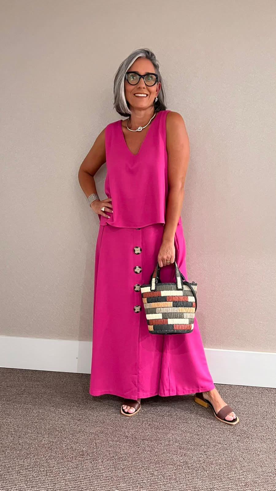 Mulher usando conjunto de saia e regata rosa, sandália e bolsa de palha colorida, em ambiente interno EZILDINHA