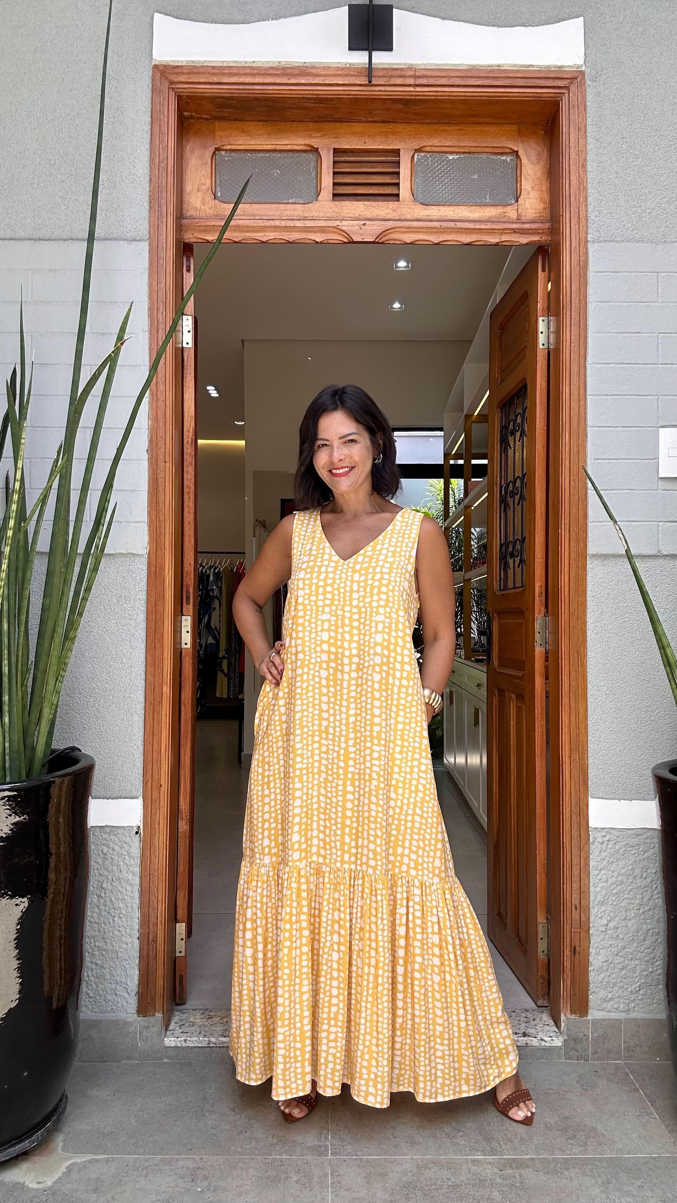 Mulher usando vestido longo amarelo estampado, estilo kaftan, em porta de loja elegante EZILDINHA