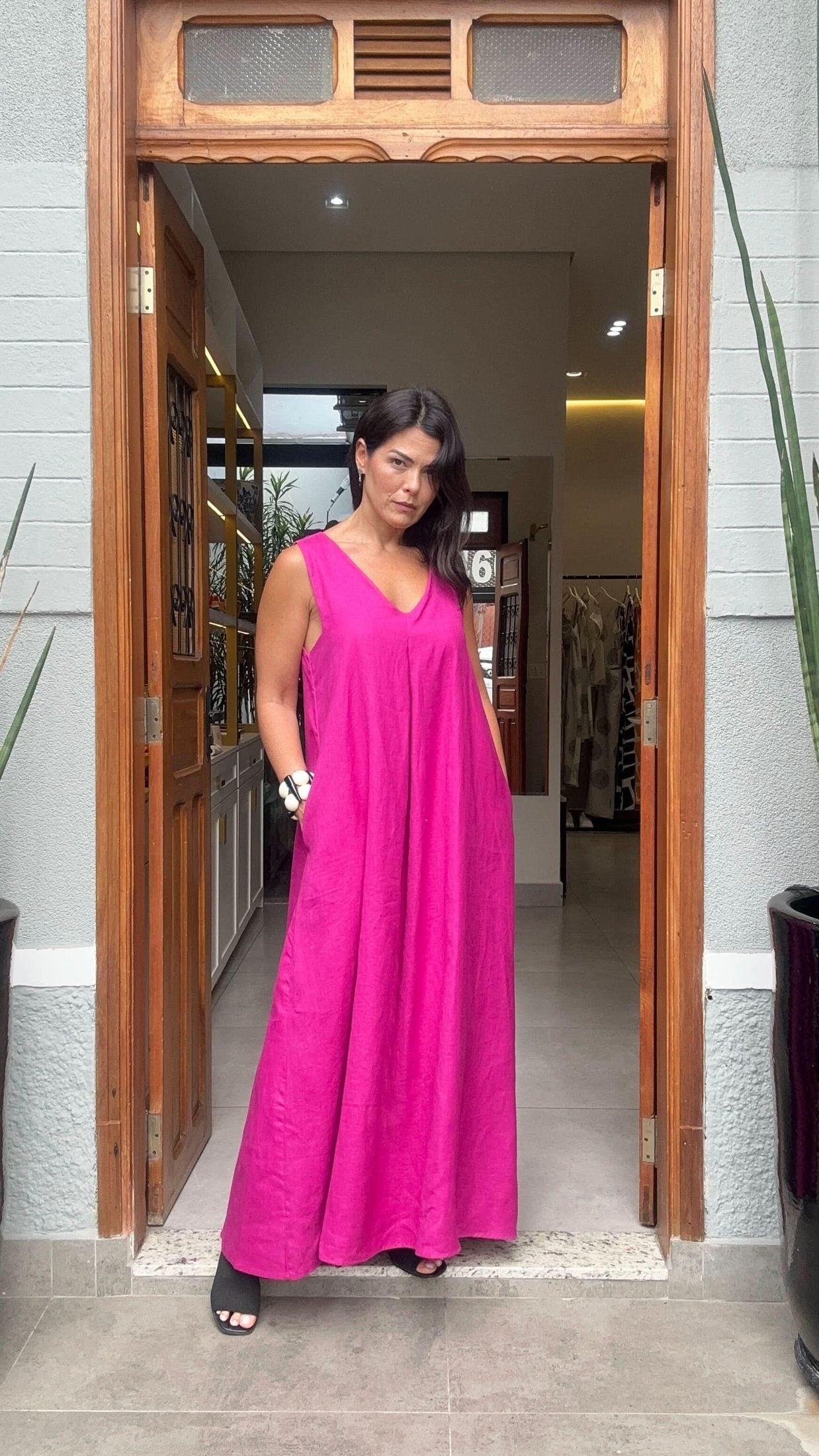 Mulher usando vestido longo de linho rosa, decote em V, em porta de loja elegante EZILDINHA