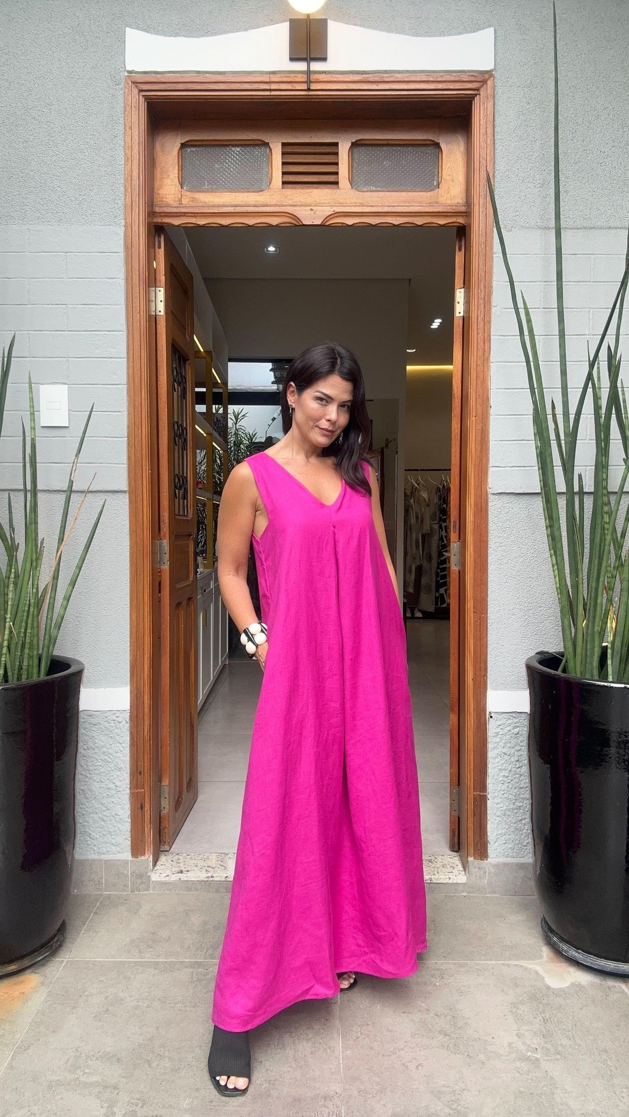 Mulher usando vestido longo rosa de linho, decote V, em entrada de loja elegante EZILDINHA
