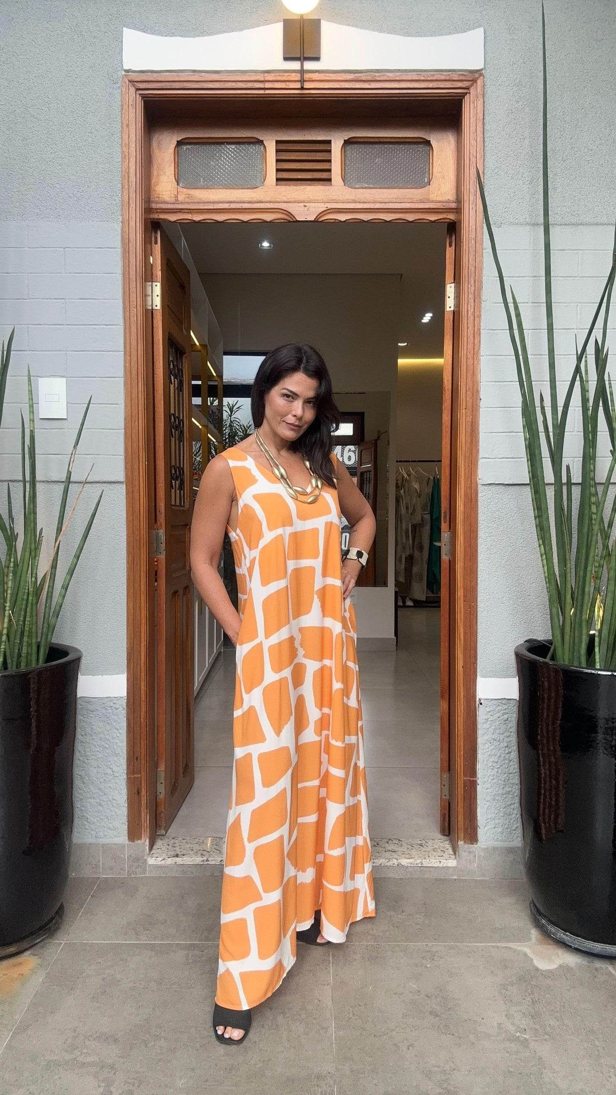 Mulher usando vestido longo laranja e branco estampado, modelo kaftan, em porta de loja EZILDINHA