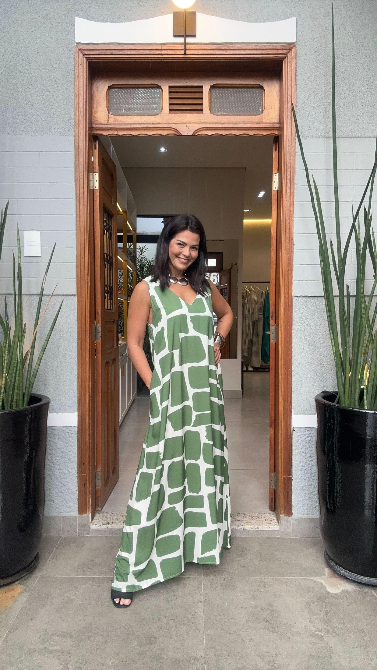 Mulher usando vestido longo verde e branco estampado, modelagem ampla, em ambiente externo elegante EZILDINHA