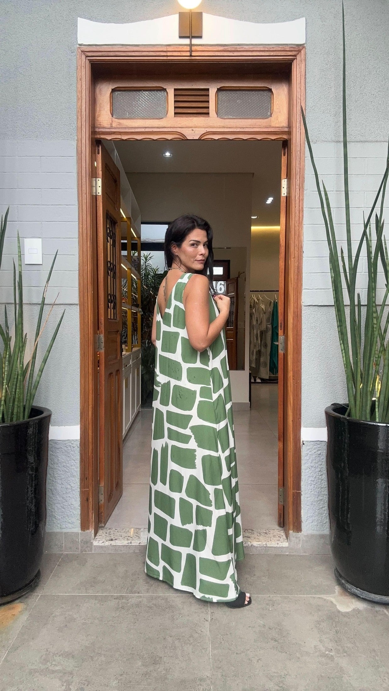 Mulher usando kaftan longo estampado verde e branco, em frente a porta de loja EZILDINHA
