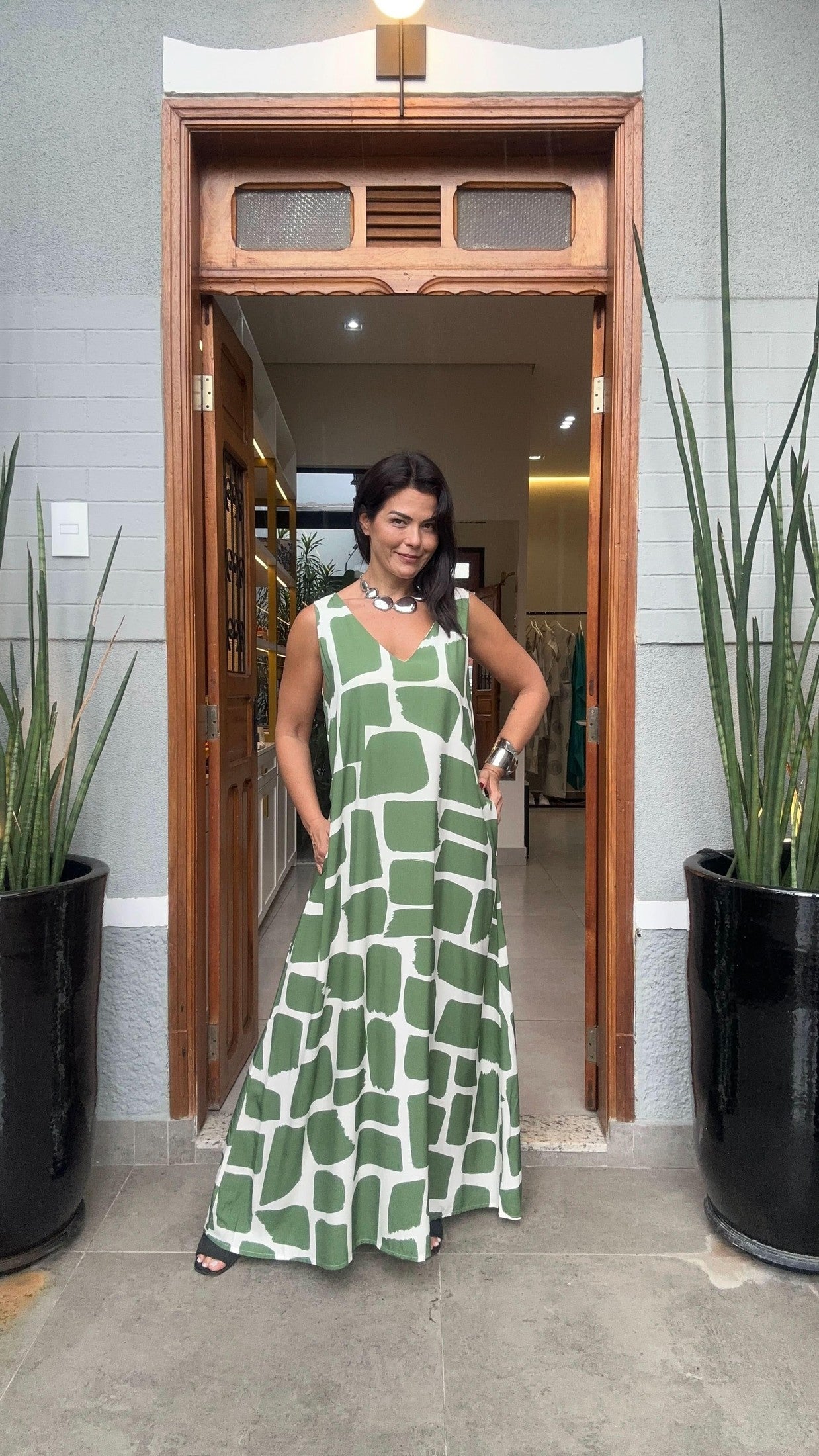 Mulher usando vestido longo de seda verde e branco com estampa geométrica, em entrada de casa EZILDINHA