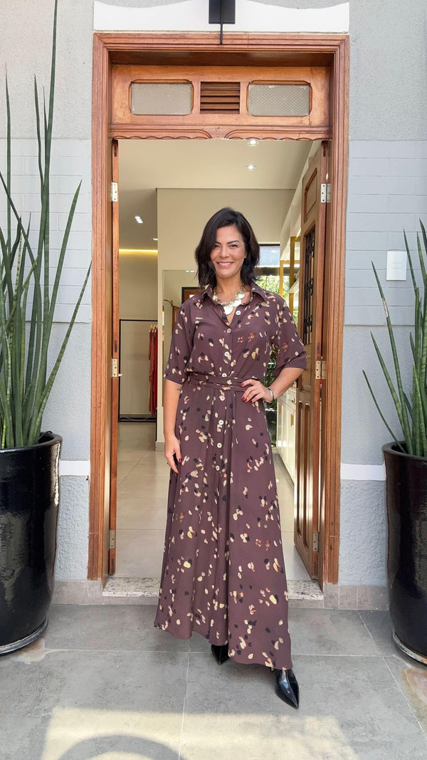 Mulher sorrindo usa vestido longo estampado marrom de seda na entrada de uma loja elegante EZILDINHA