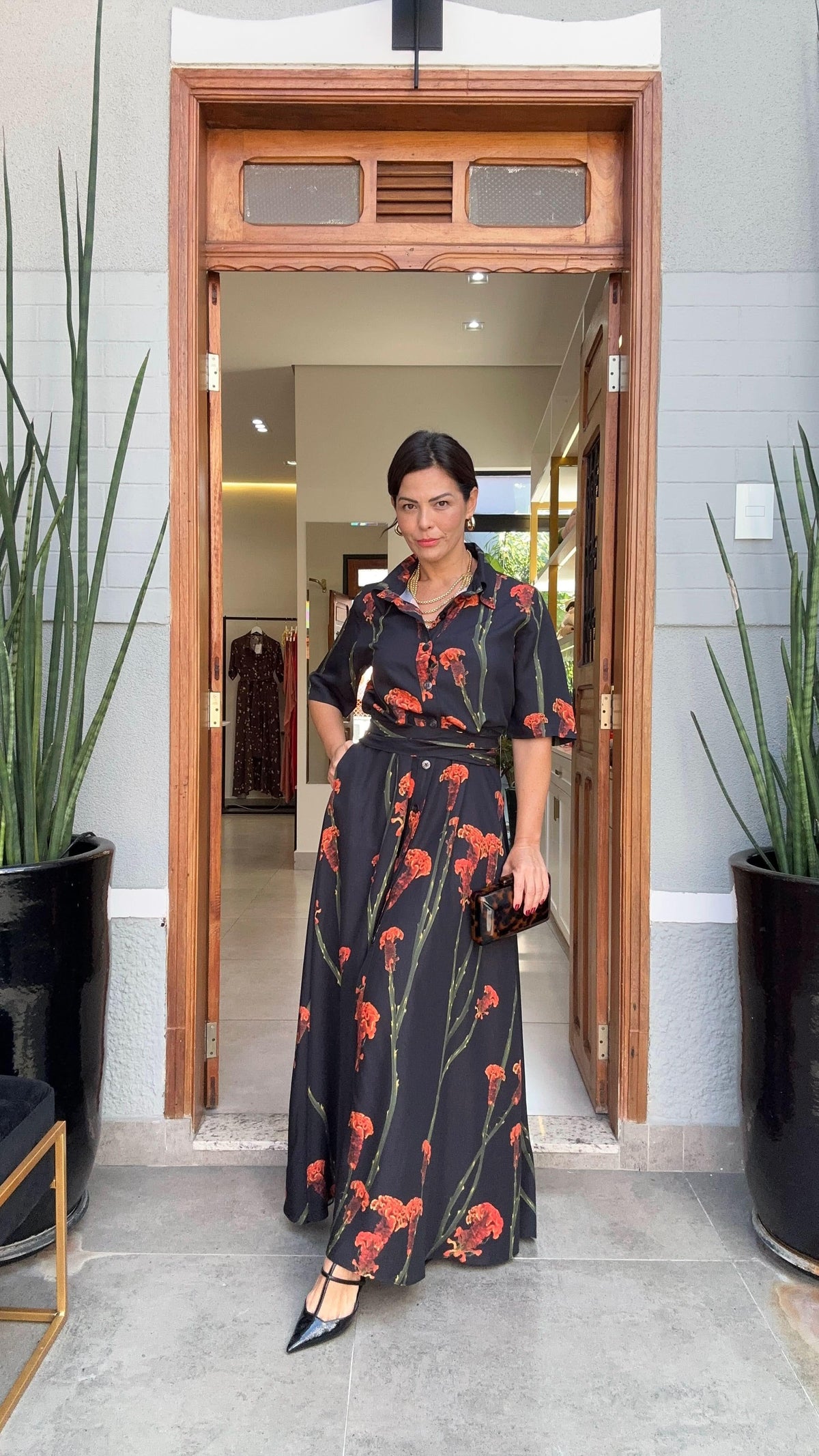 Mulher usando vestido longo preto com estampa floral vermelha, elegante na porta de loja EZILDINHA