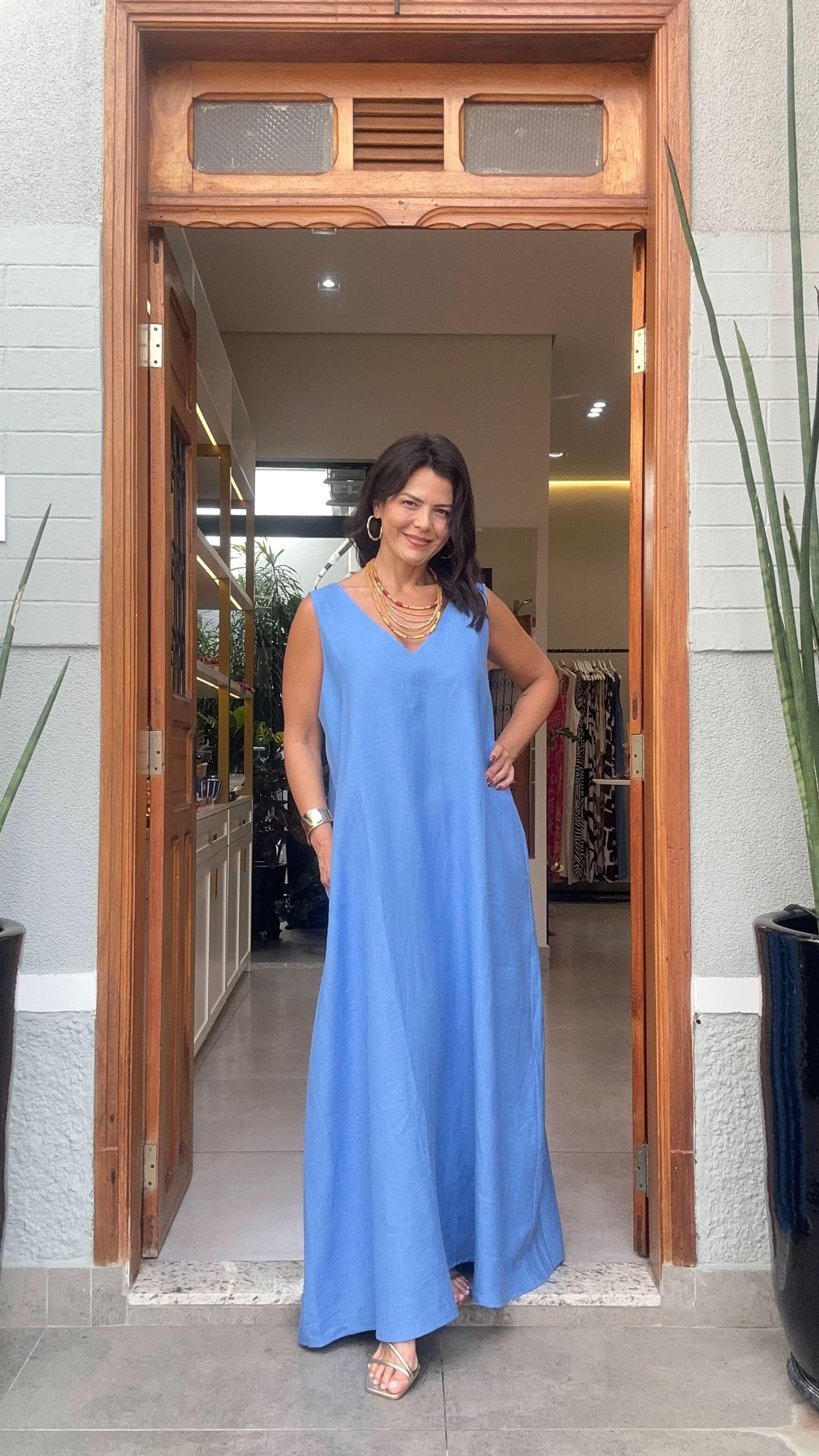 Mulher usando vestido longo azul de linho, em frente a porta de loja de moda feminina EZILDINHA