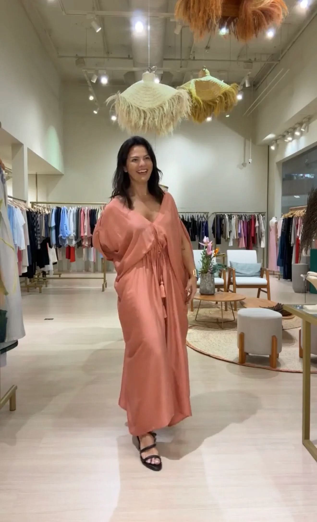 Mulher vestindo kaftan longo salmão em loja de roupas elegantes, ambiente moderno EZILDINHA