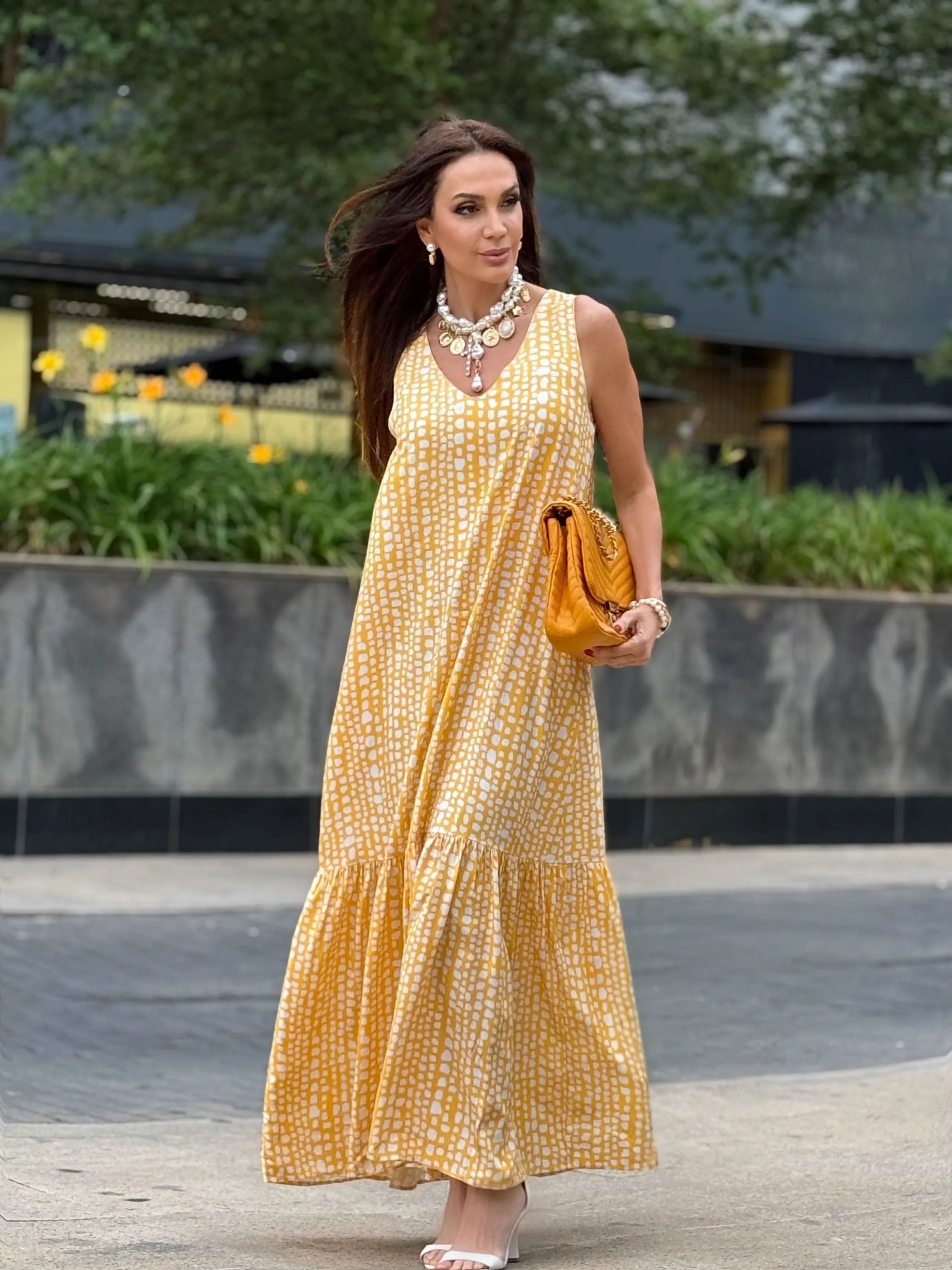 Mulher usando vestido longo amarelo estampado de linho, bolsa amarela e sandálias brancas ao ar livre EZILDINHA