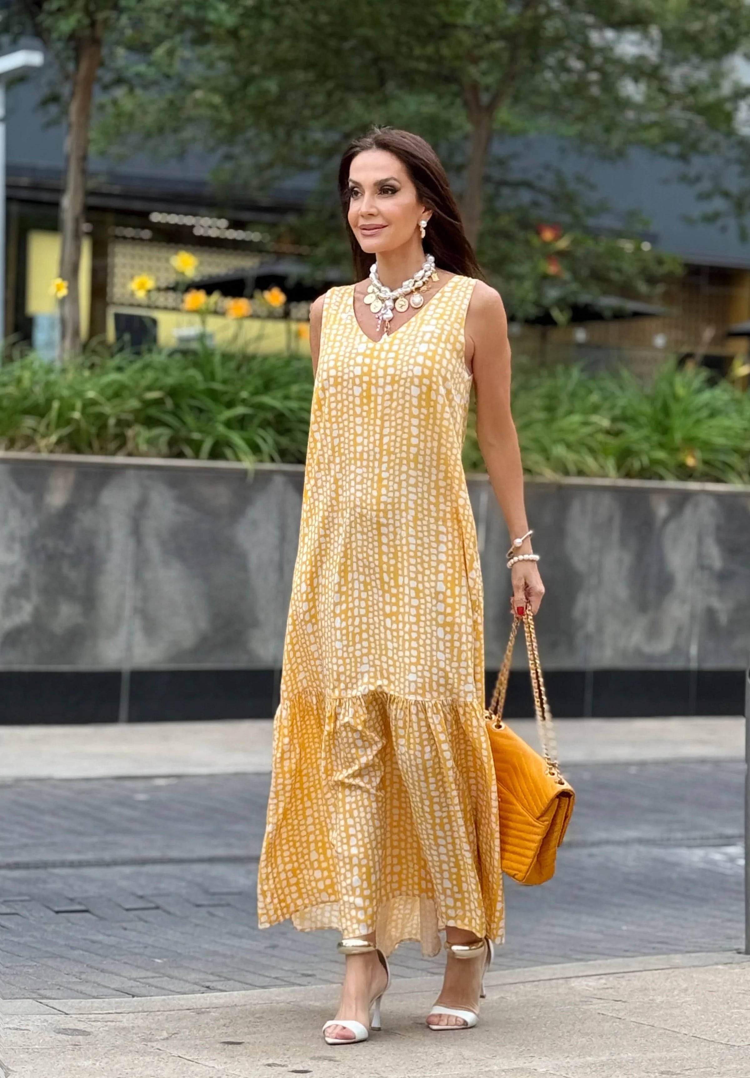 Mulher usa vestido longo amarelo estampado de seda, sandálias brancas e bolsa amarela na rua EZILDINHA