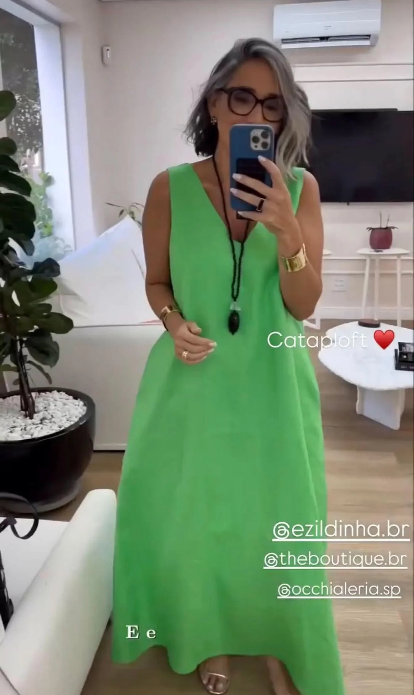 Mulher com cabelos grisalhos usando vestido longo verde de linho em sala moderna, tirando selfie EZILDINHA