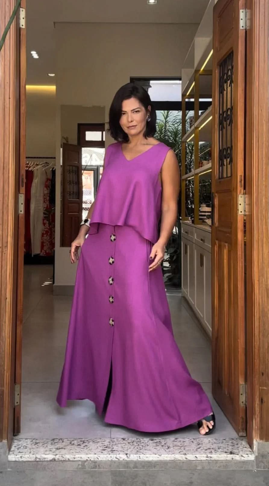 Mulher vestindo conjunto de blusa e saia longa roxa com botões, em ambiente interno elegante EZILDINHA