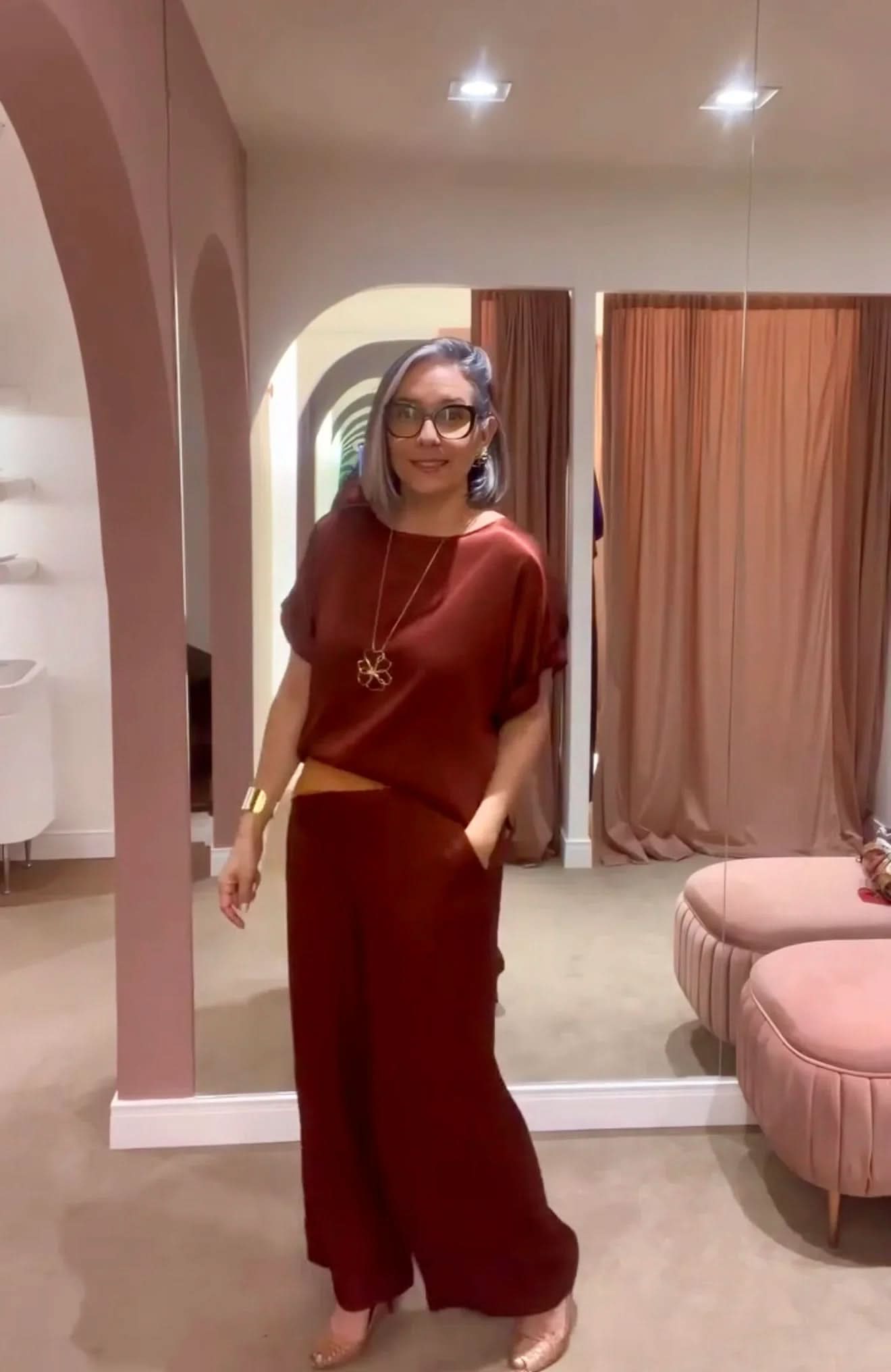 Mulher com cabelo curto usando conjunto de seda marrom, em provador elegante com espelhos EZILDINHA