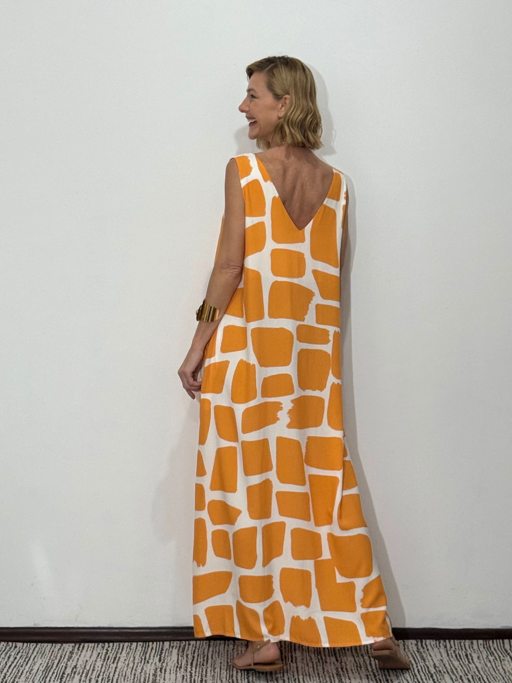 Mulher usando vestido longo estampado geométrico laranja e branco, de costas, em ambiente interno EZILDINHA