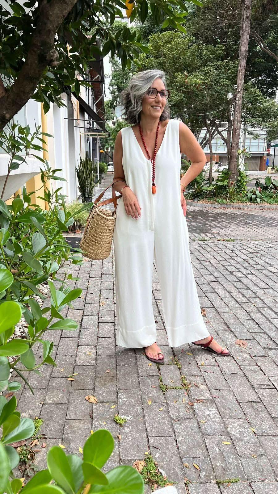 Mulher usando macacão branco de linho com zíper, sandália e bolsa de palha, ao ar livre EZILDINHA