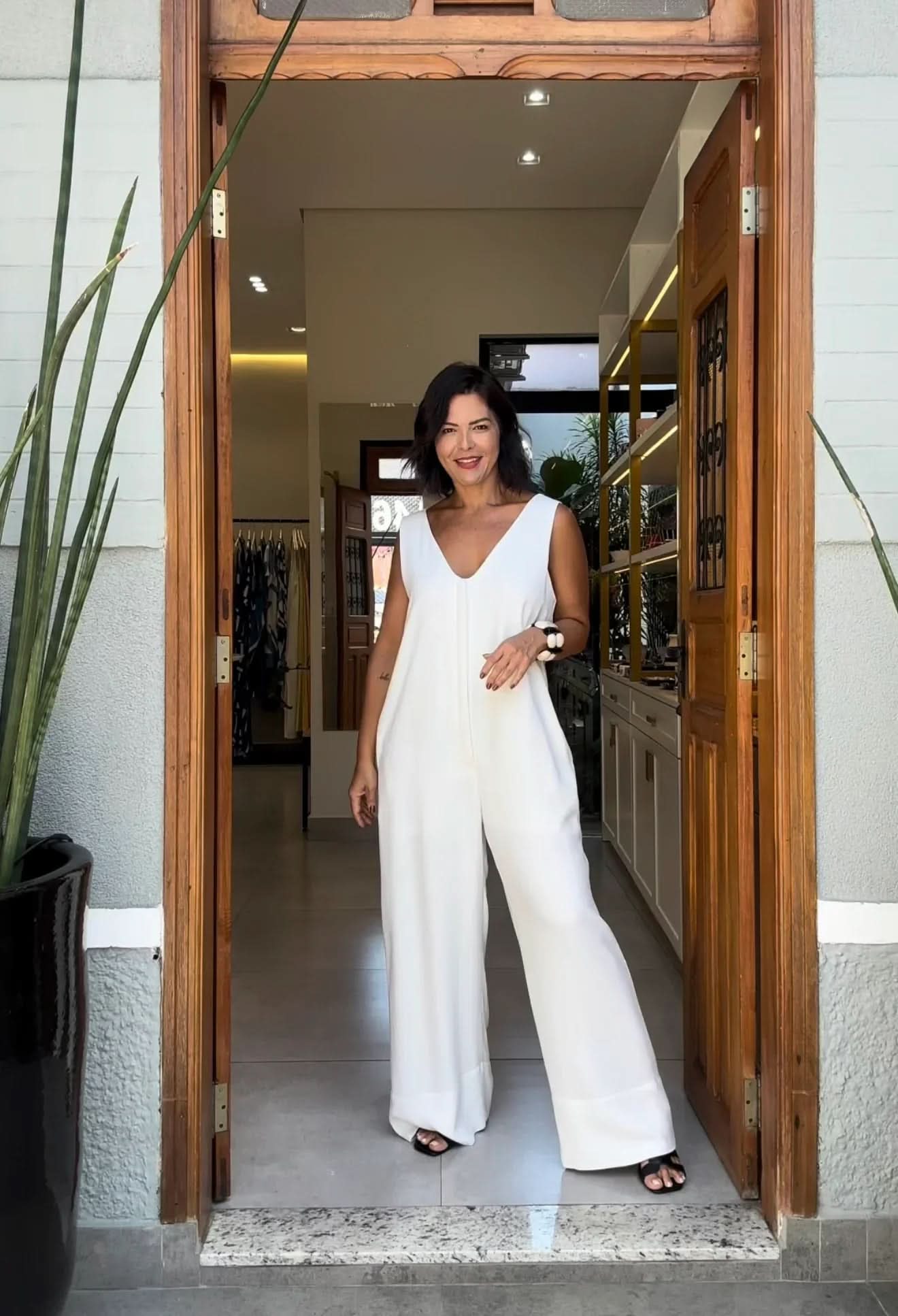 Mulher usando macacão de viscose branco com decote V, em ambiente moderno EZILDINHA