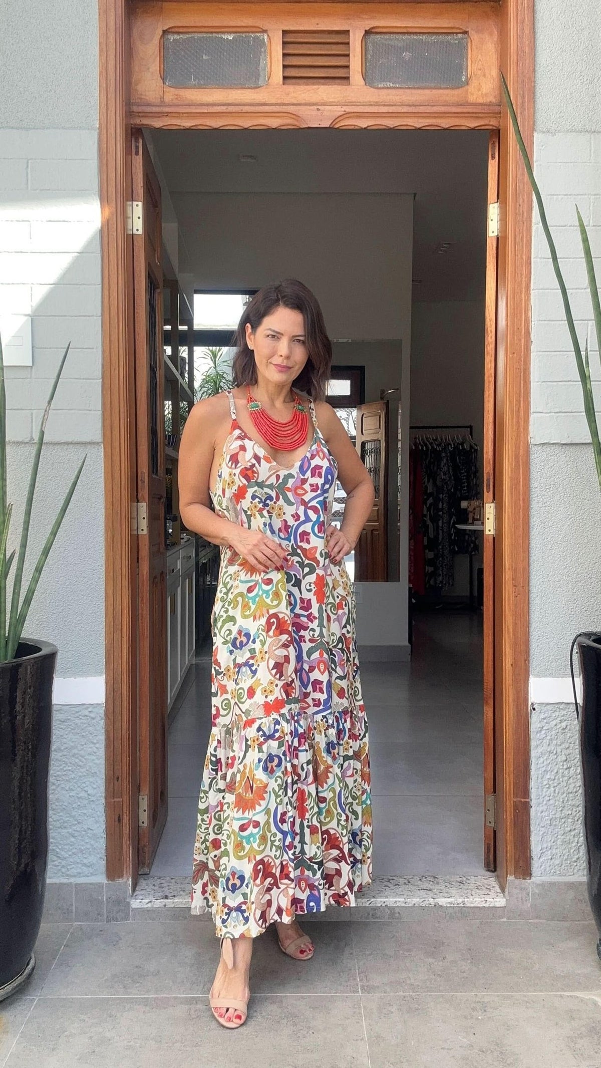 Mulher vestindo vestido longo de alças com estampa colorida floral, em porta de casa EZILDINHA