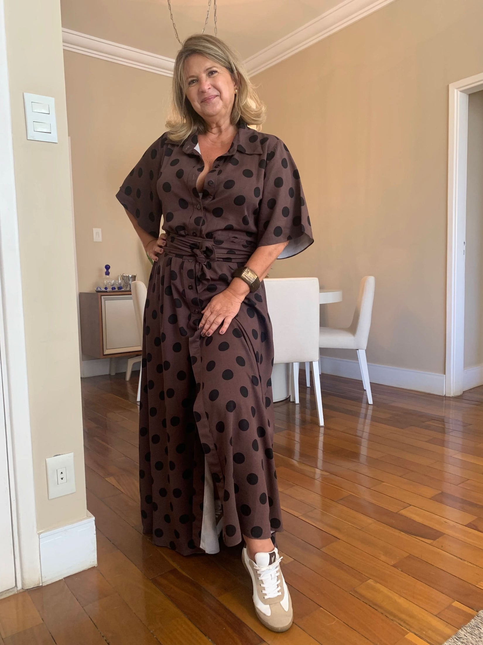 Mulher usando vestido chemisier marrom de poá, manga curta, em ambiente interno elegante EZILDINHA