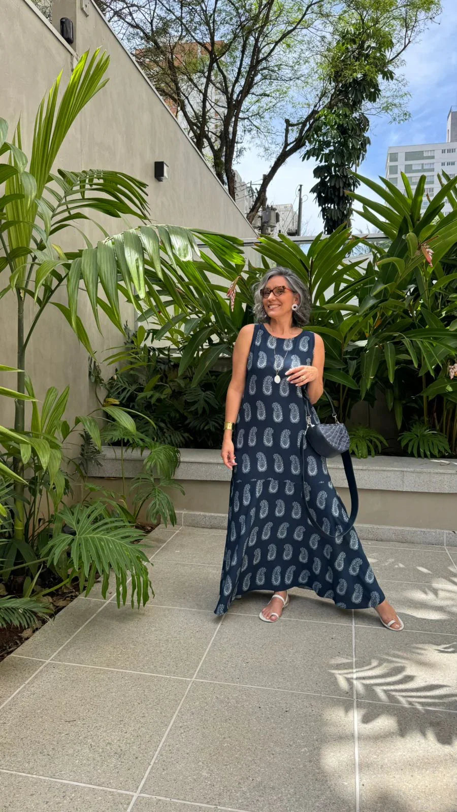 Mulher usando vestido longo azul marinho de viscose estampado, em jardim urbano com folhagens tropicais EZILDINHA