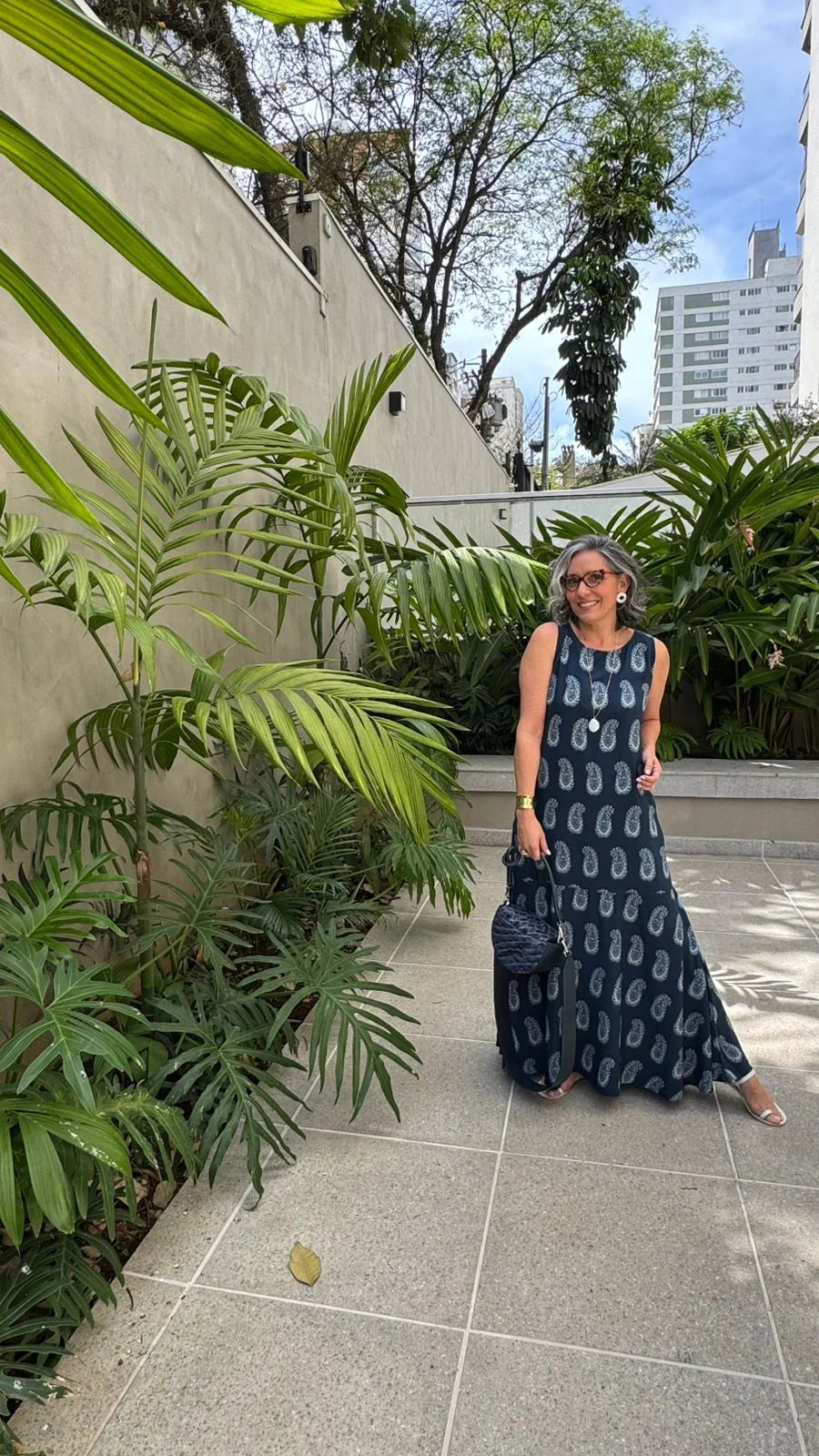 Mulher usando vestido longo azul estampado de viscose em ambiente externo com plantas tropicais EZILDINHA
