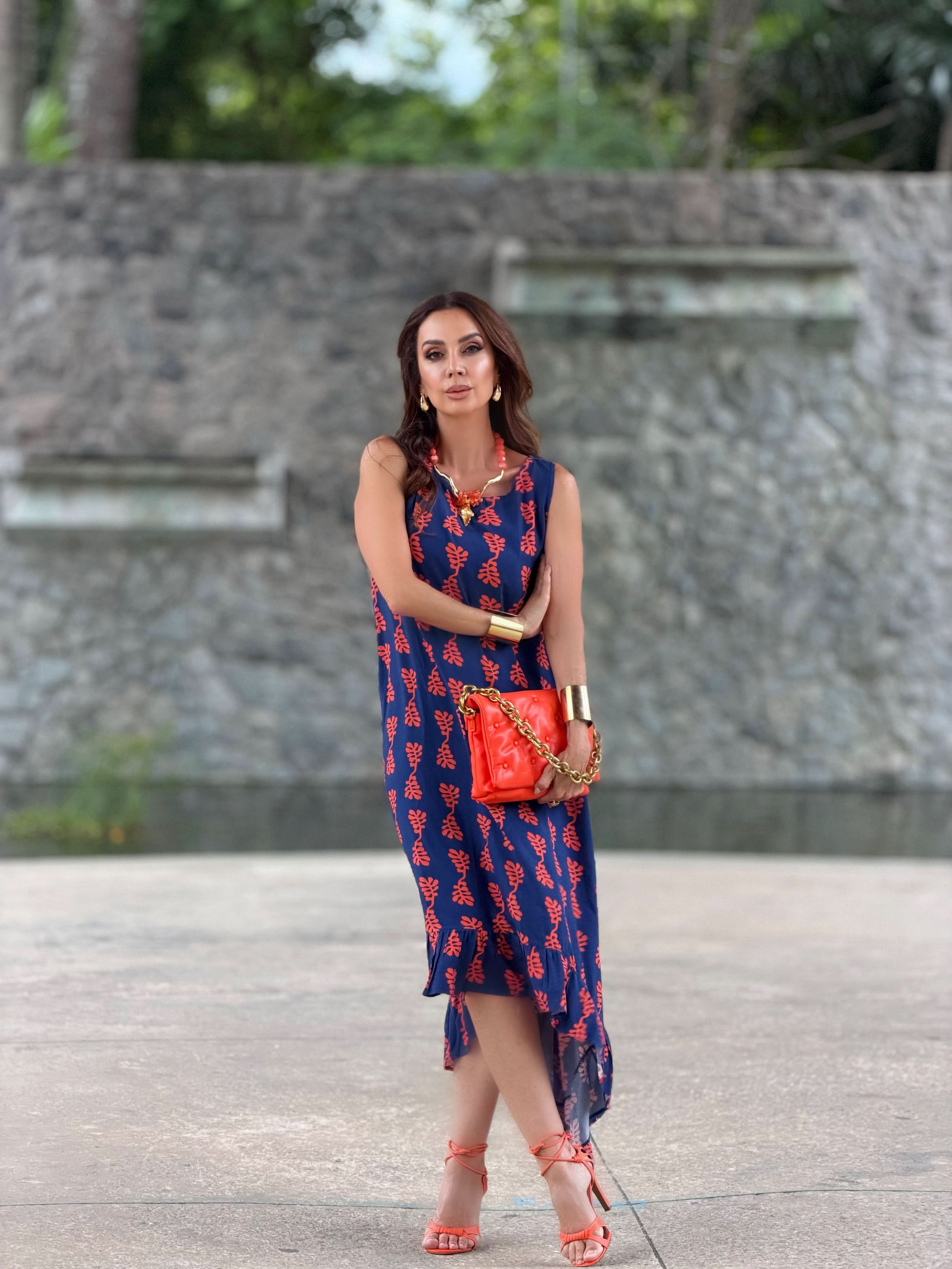 Mulher usando vestido azul estampado com folhas vermelhas, bolsa e sandálias laranja EZILDINHA