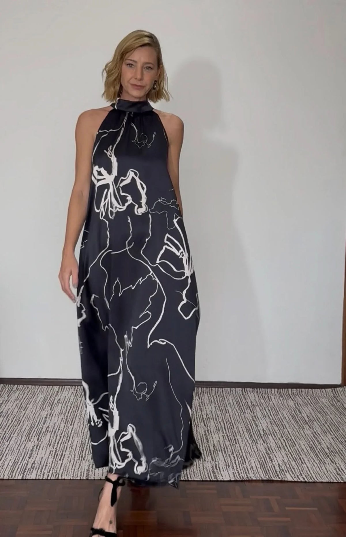 Mulher vestindo vestido longo de seda pura preto com estampa floral branca, gola laço EZILDINHA