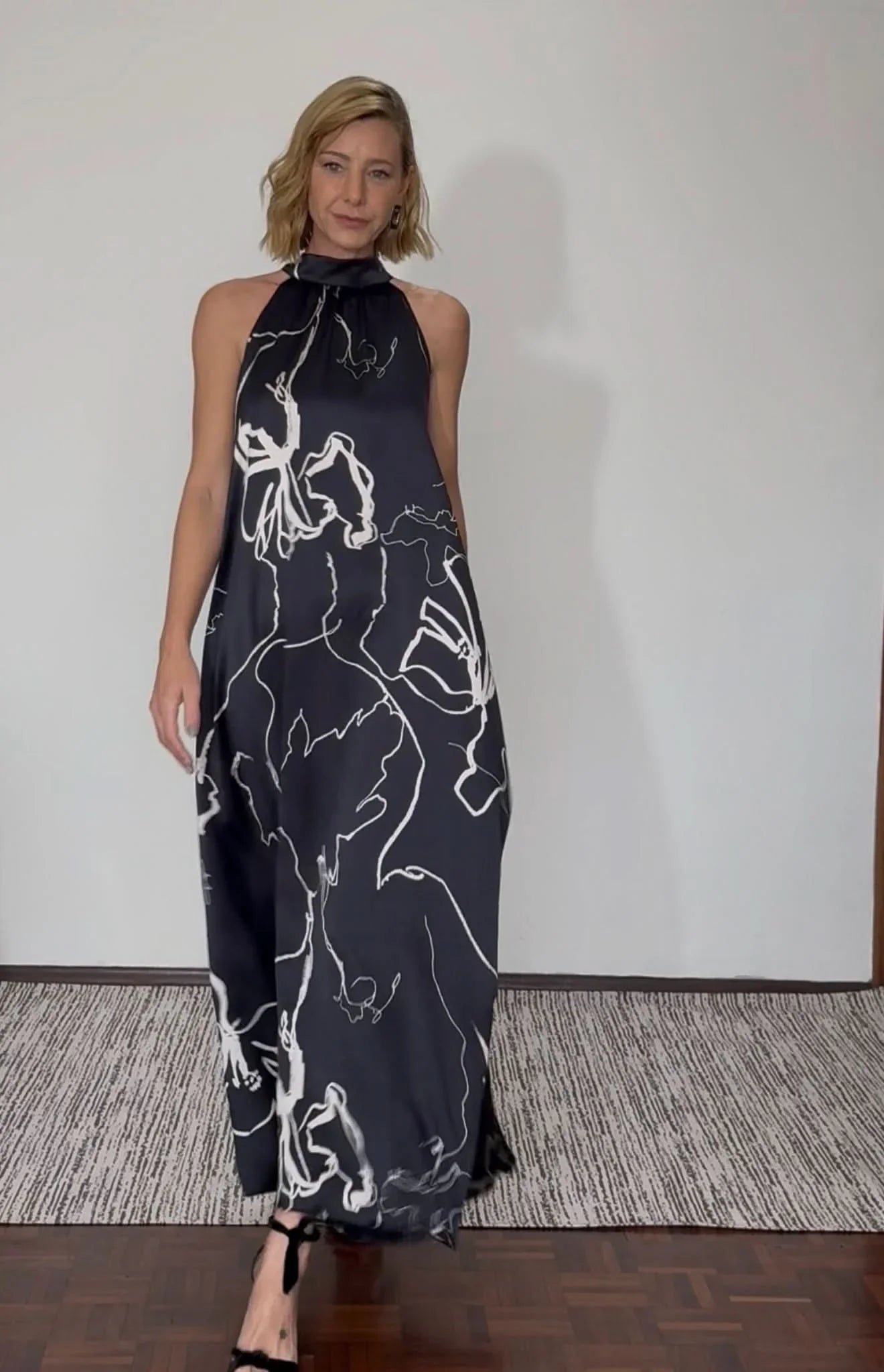 Mulher vestindo vestido longo de seda pura preto com estampa floral branca, gola laço EZILDINHA