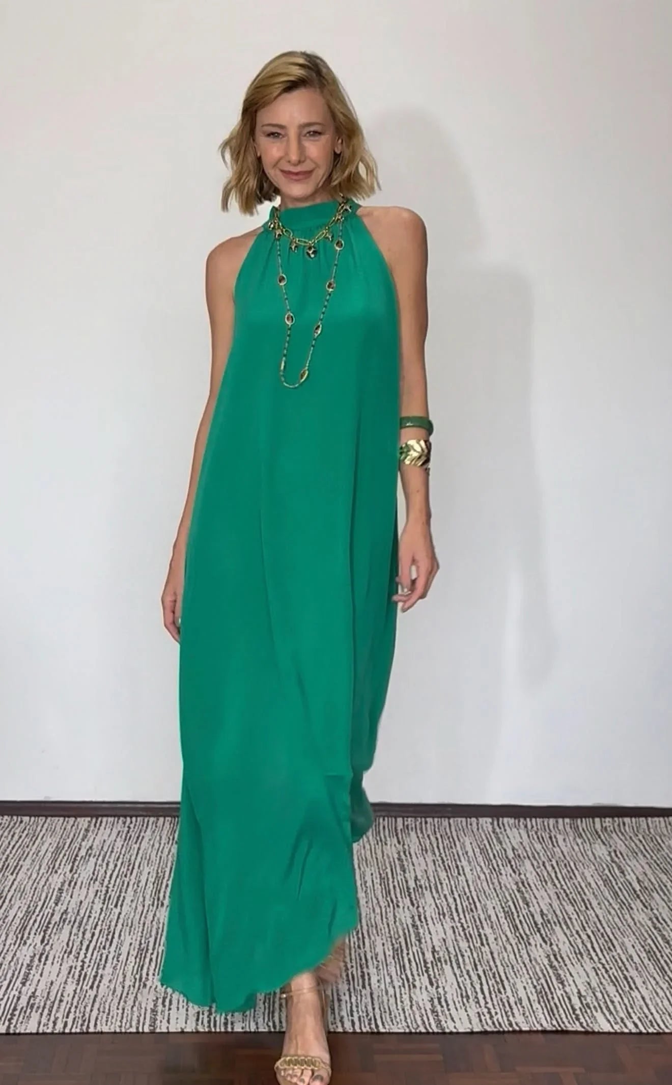 Mulher usando vestido longo verde em seda pura, sem mangas, com acessórios dourados EZILDINHA