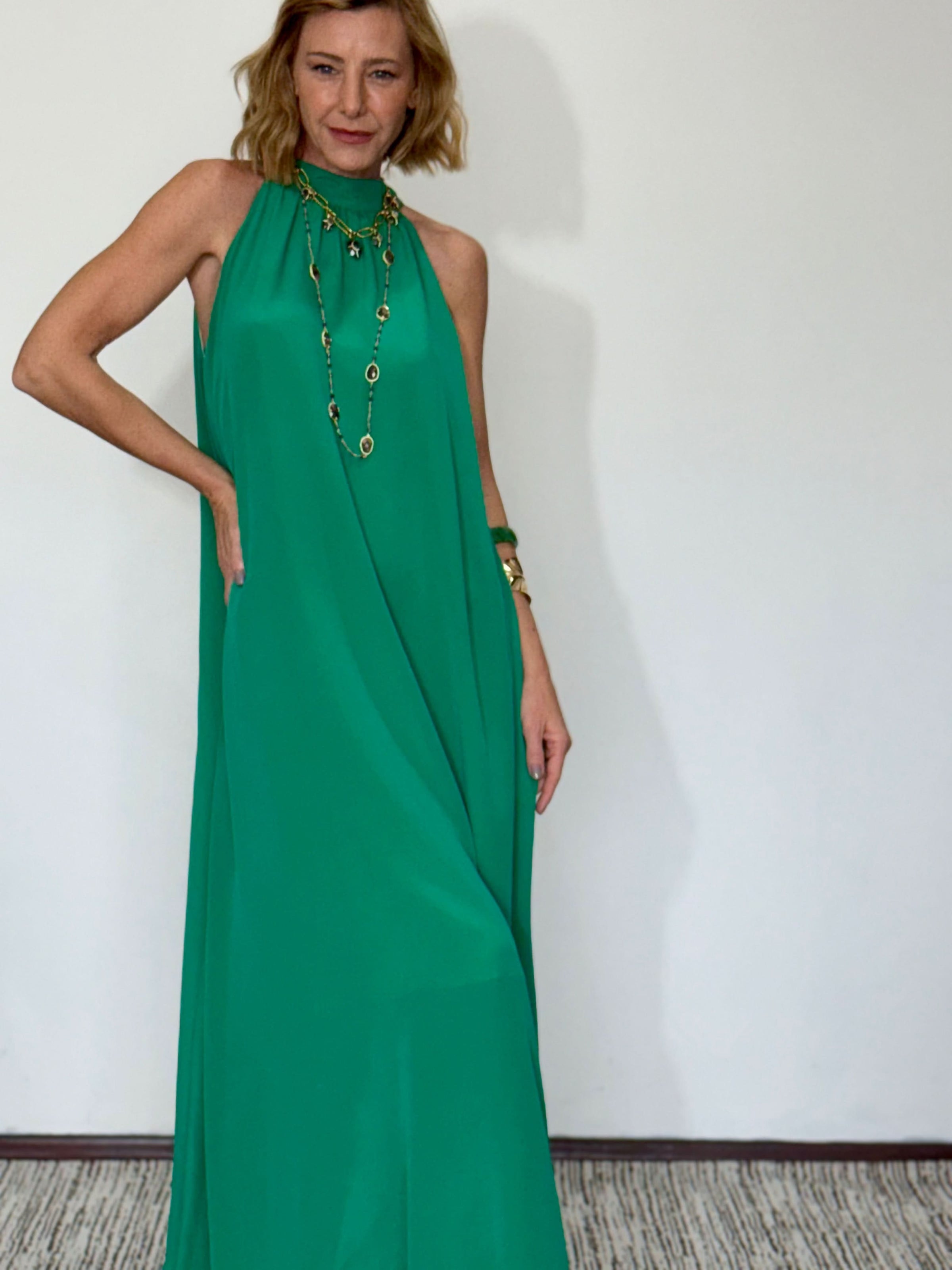 Mulher usando vestido longo em seda pura verde, com decote alto e acessórios dourados EZILDINHA