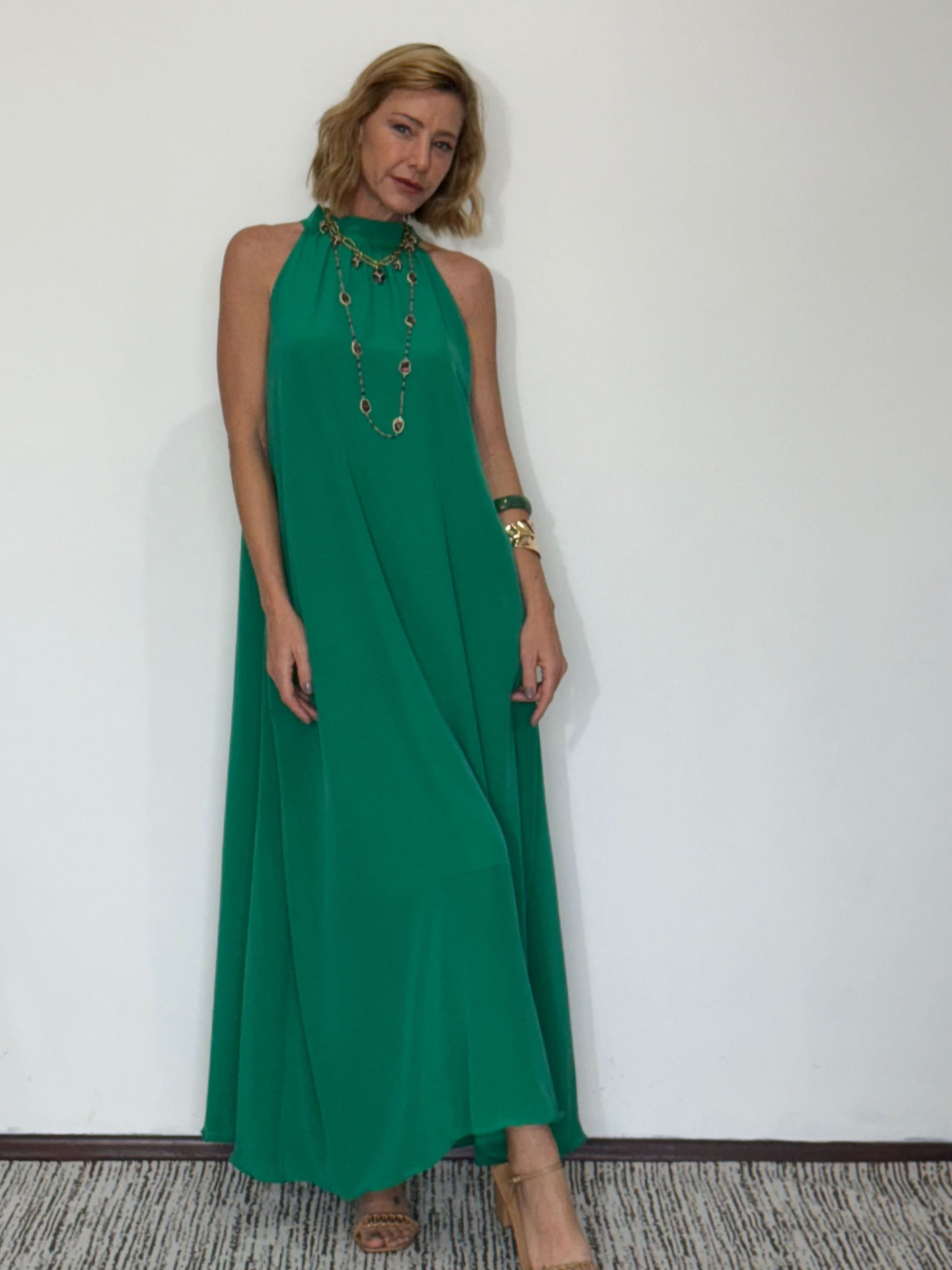 Mulher usando vestido longo verde de seda pura com gola alta, acessórios dourados, fundo branco EZILDINHA