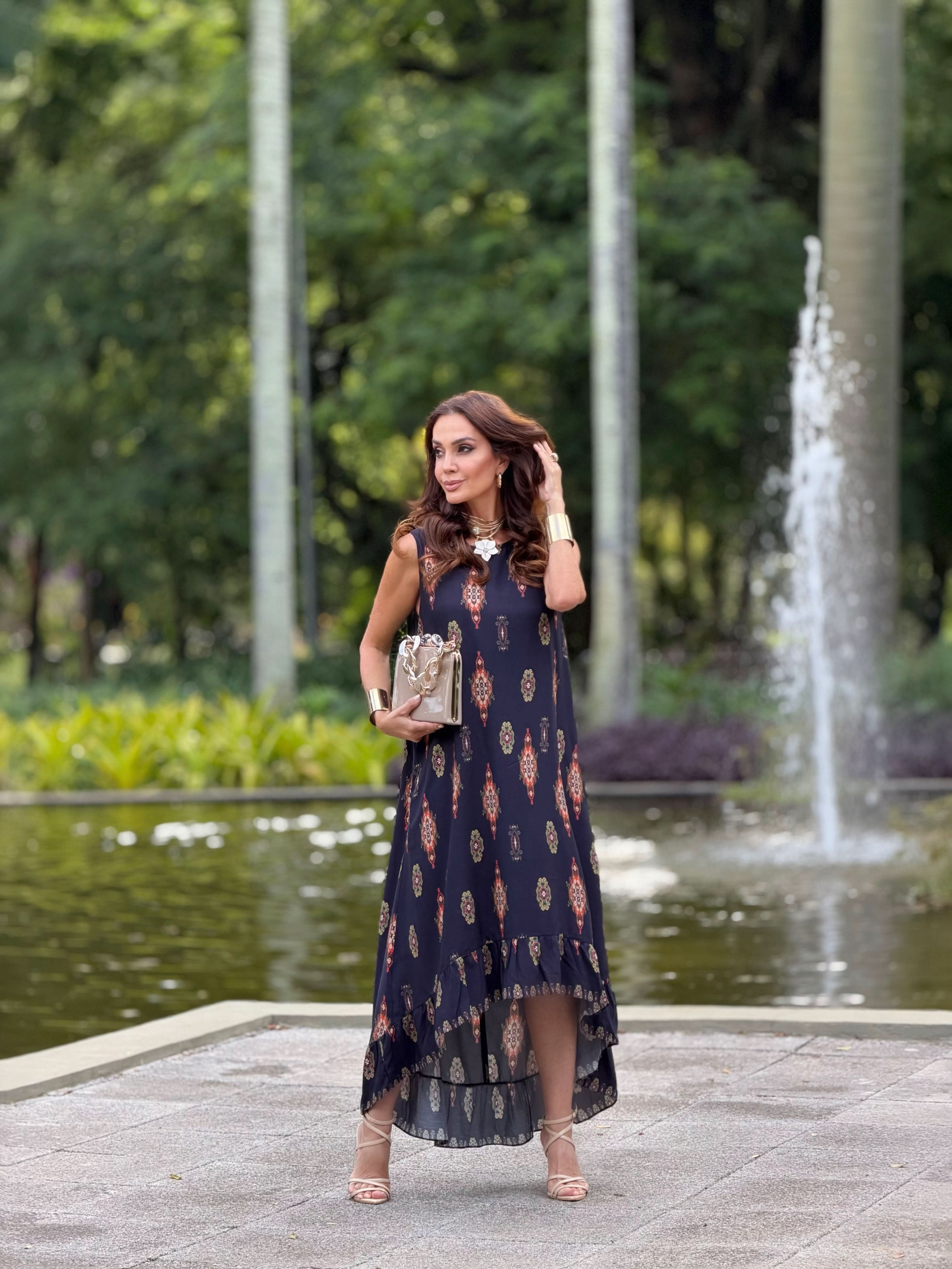Mulher usando vestido longo de viscose estampado em ambiente externo com fonte e vegetação ao fundo EZILDINHA