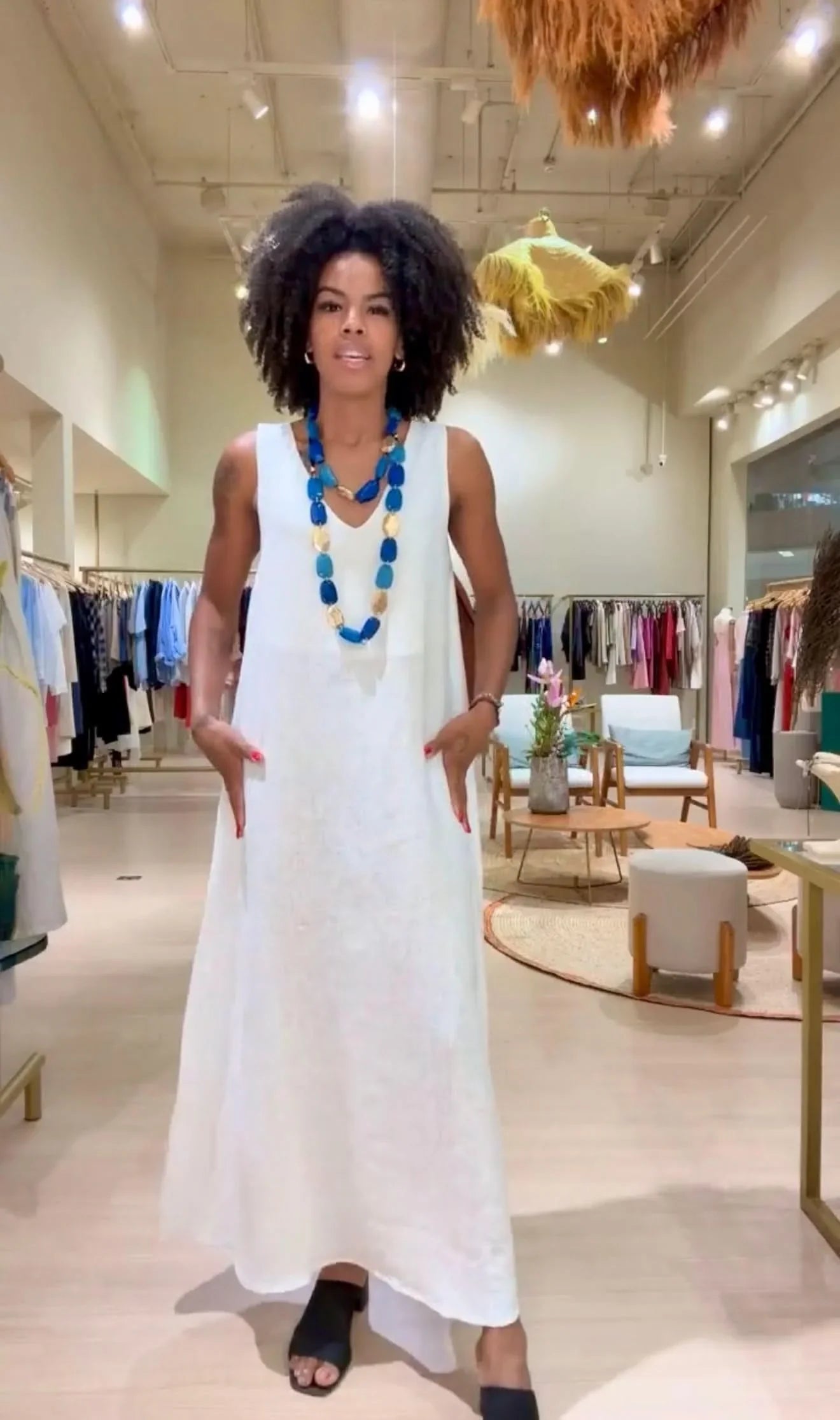 Mulher usando vestido longo de linho off-white, decote V, colar azul, em loja de moda feminina EZILDINHA