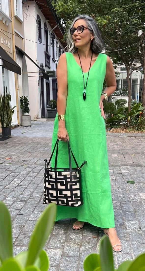 Mulher usando vestido longo verde de linho, bolsa preta e branca e acessórios, em ambiente urbano EZILDINHA