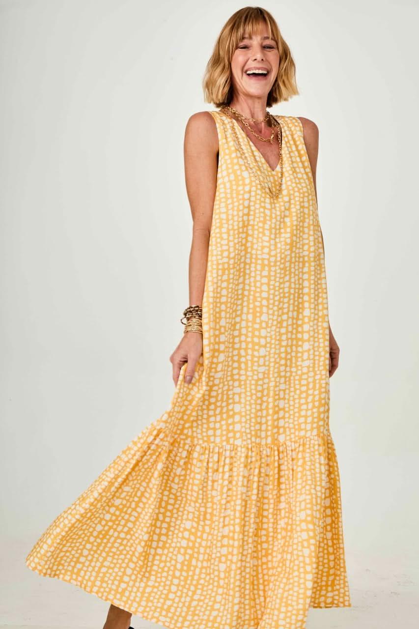 Mulher usando vestido longo amarelo com estampa geométrica, sem mangas, em fundo neutro EZILDINHA