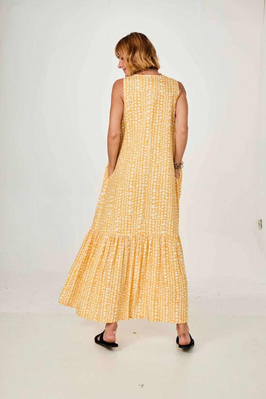 Mulher de costas vestindo vestido longo amarelo com estampa geométrica e sandálias pretas EZILDINHA