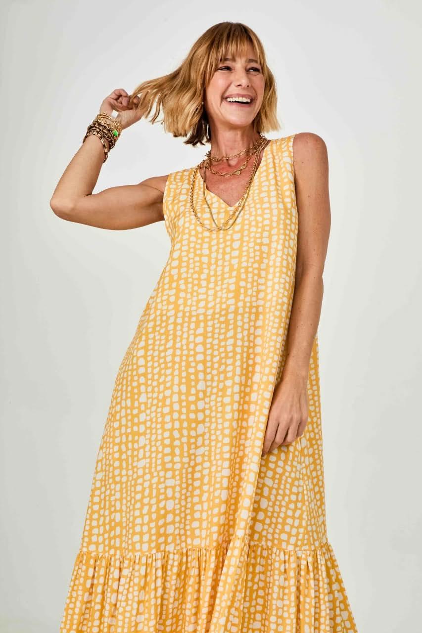 Mulher sorridente usando vestido longo amarelo com estampa geométrica e babado na barra EZILDINHA
