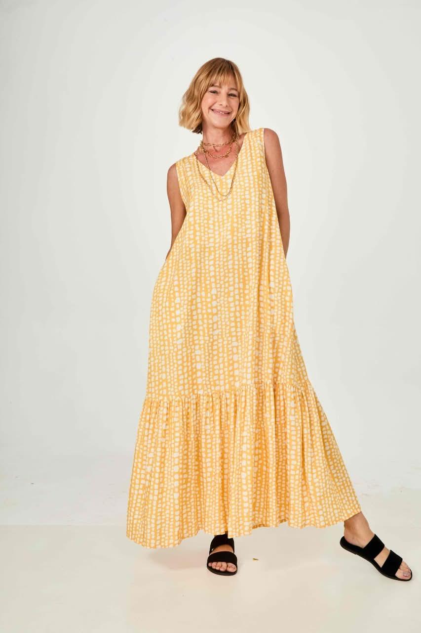 Mulher sorrindo usando vestido longo amarelo estampado, sem mangas, em fundo neutro EZILDINHA