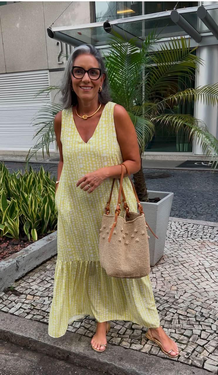 Mulher com vestido longo amarelo e branco estampado, bolsa de palha e sandália dourada, ao ar livre EZILDINHA
