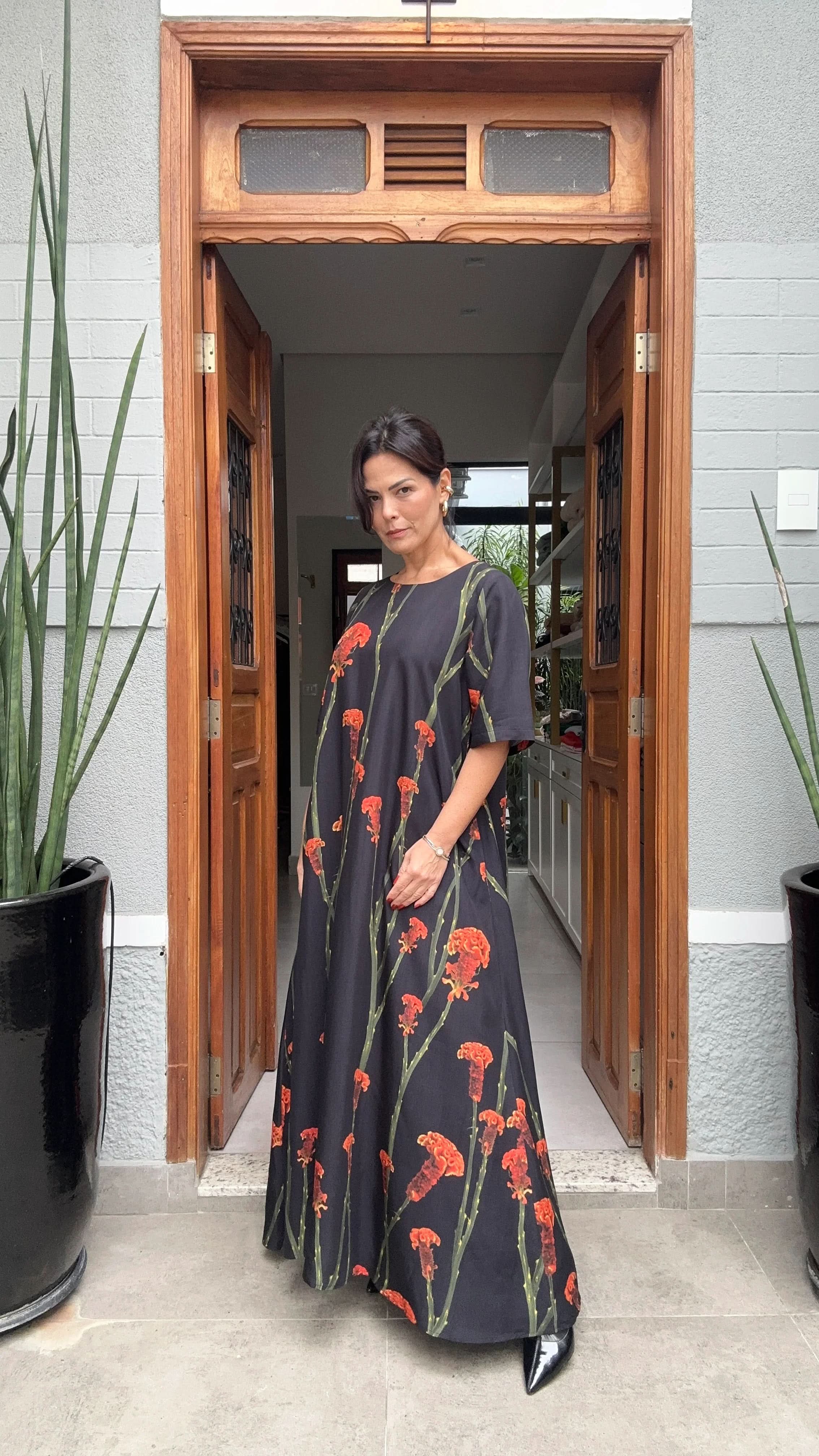 Mulher usando vestido longo preto tipo t-shirt com estampa maxi floral vermelha, em ambiente externo elegante EZILDINHA
